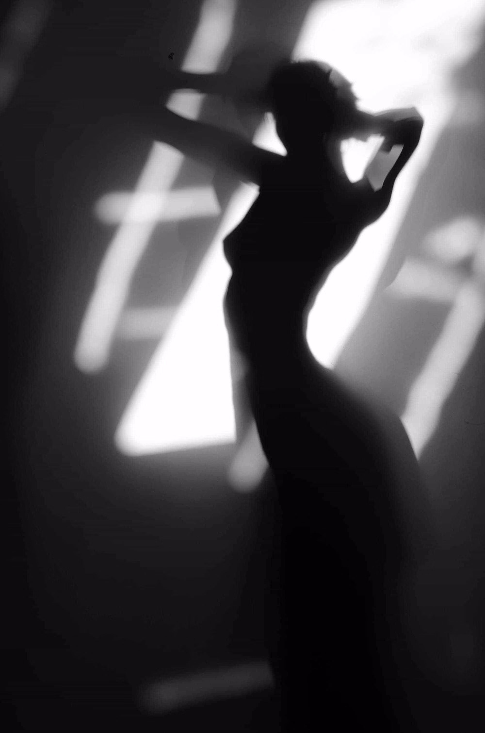 Silhouette floue d'une femme debout avec les bras levés devant une source lumineuse abstraite.