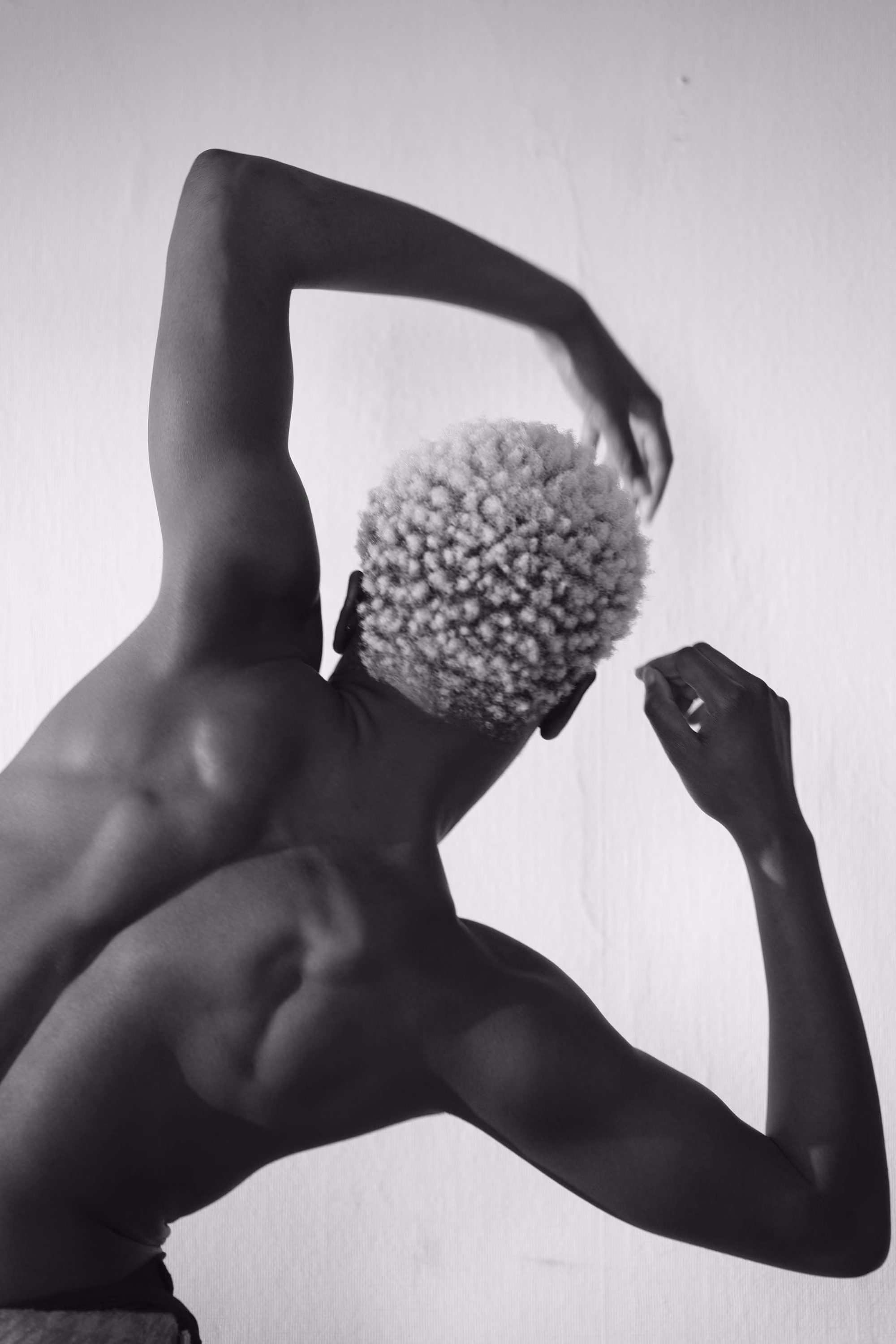 Dos nu d'une personne aux cheveux blonds bouclés, bras levés dans un geste fluide.