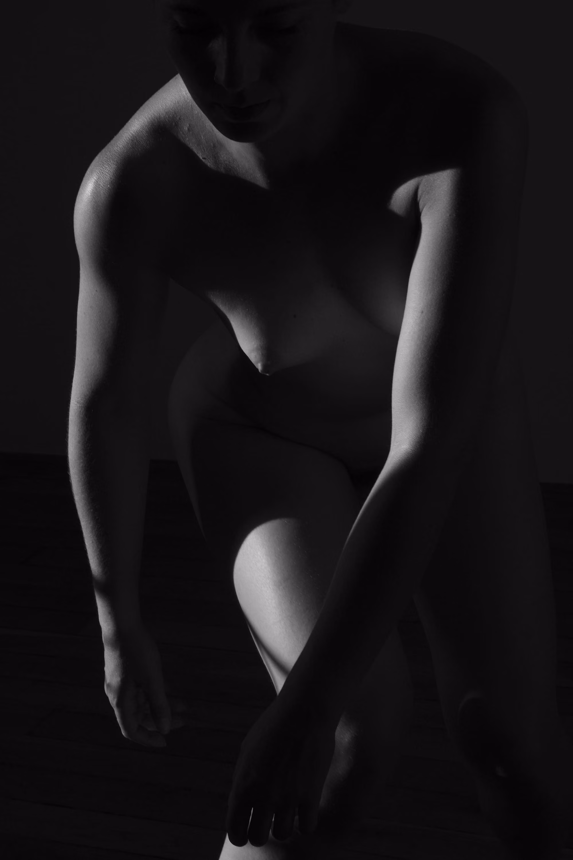 Silhouette d'une femme nue en position accroupie avec des ombres fortes et un éclairage dramatique.