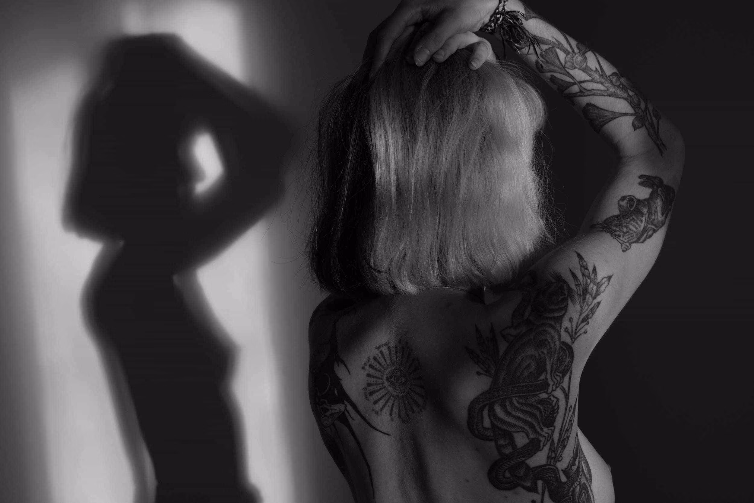 Dos d'une femme tatouée avec cheveux courts et ombre projetée sur un mur en arrière-plan.