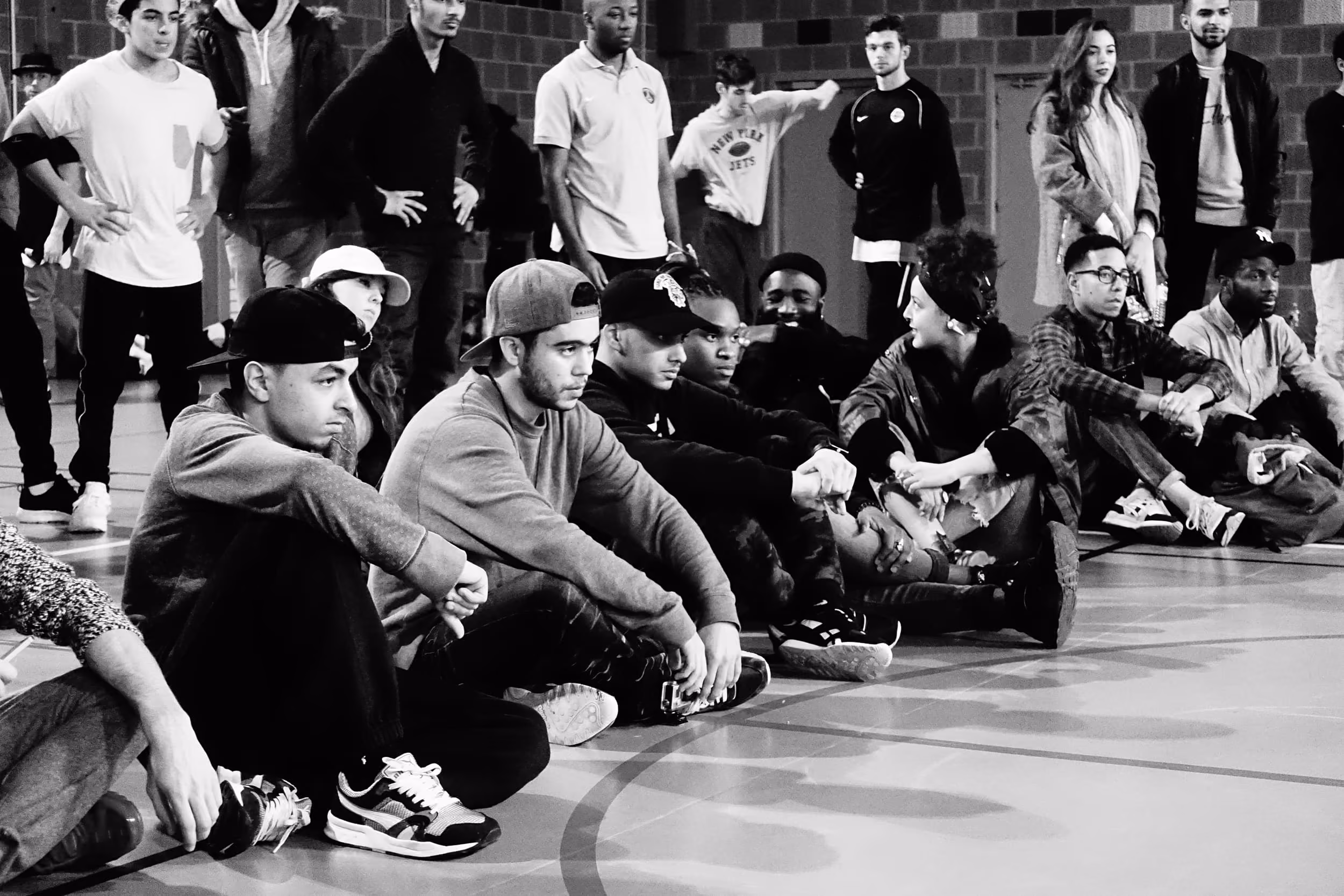 Groupe de jeunes assis et debout dans un gymnase lors d'un événement social ou sportif.
