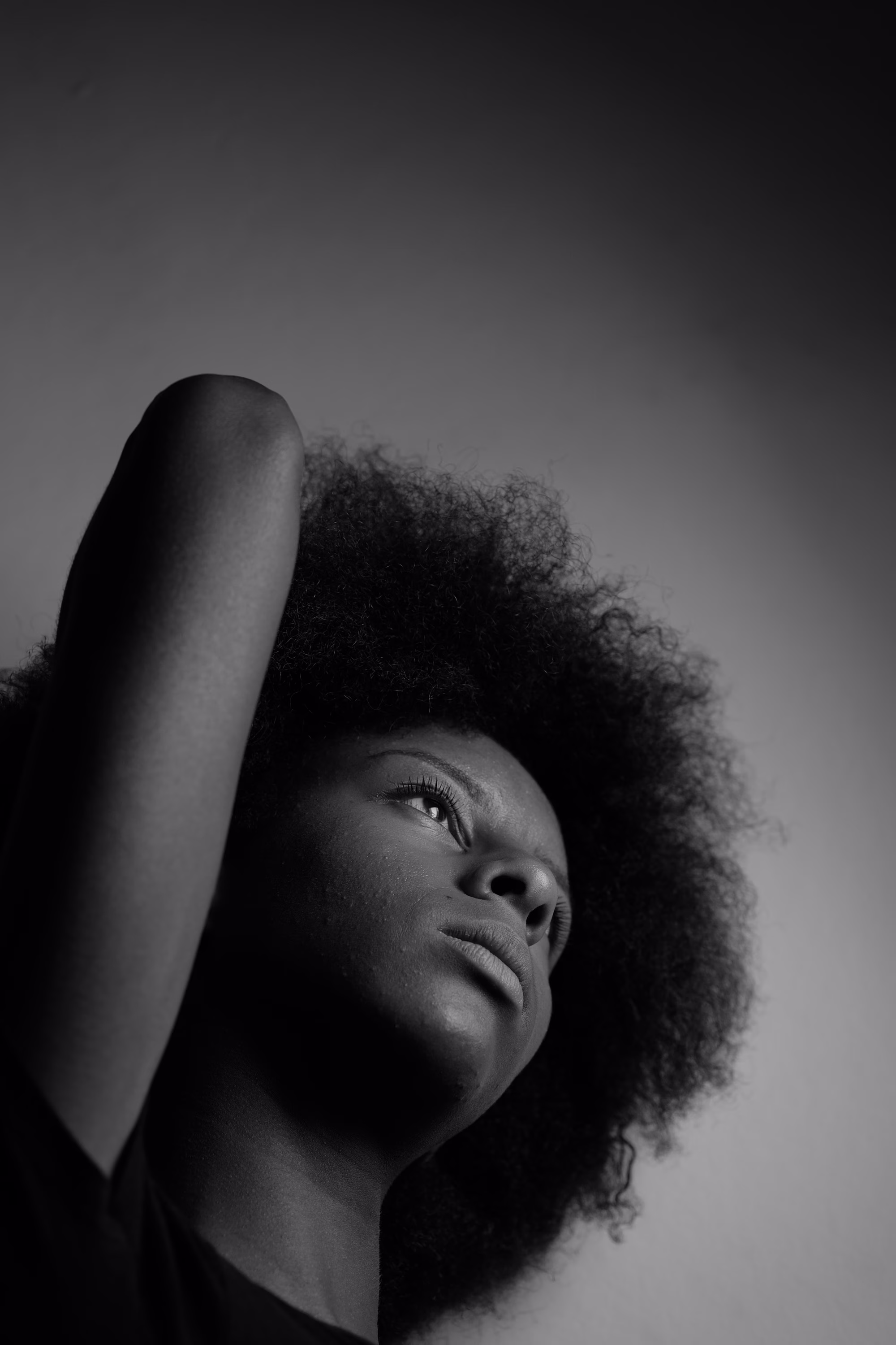 Portrait en noir et blanc d'une femme afro regardant vers le haut avec son bras levé.