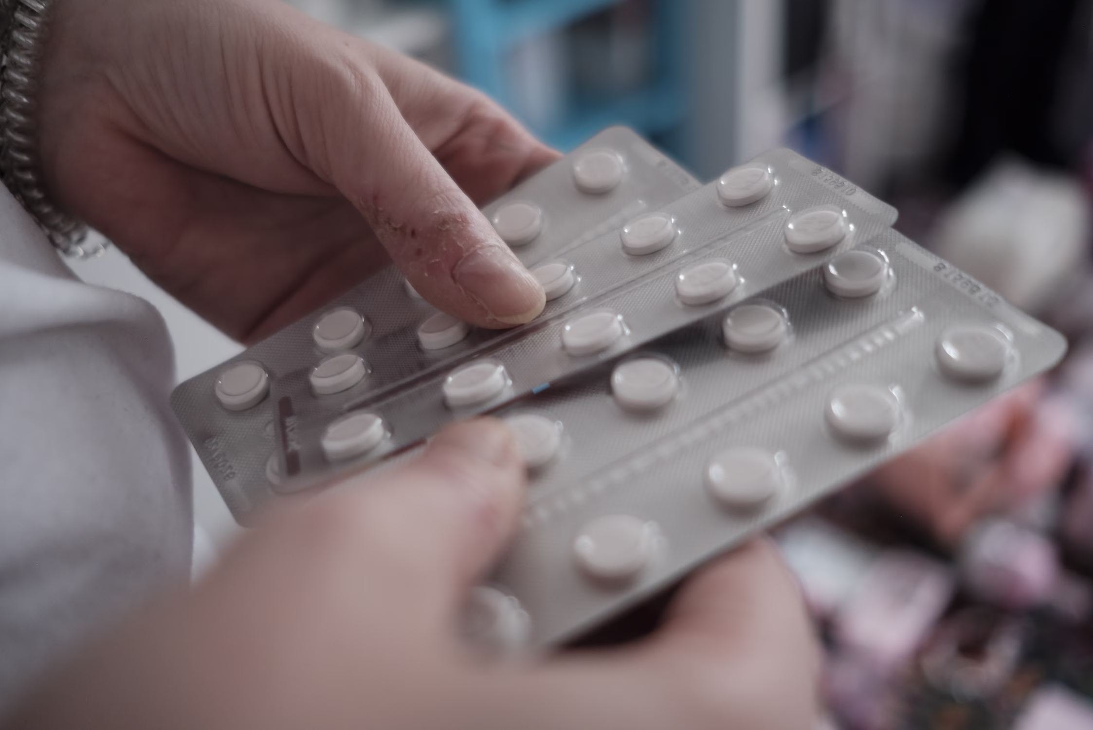 Mains tenant plusieurs plaquettes de médicaments avec des comprimés blancs ronds.