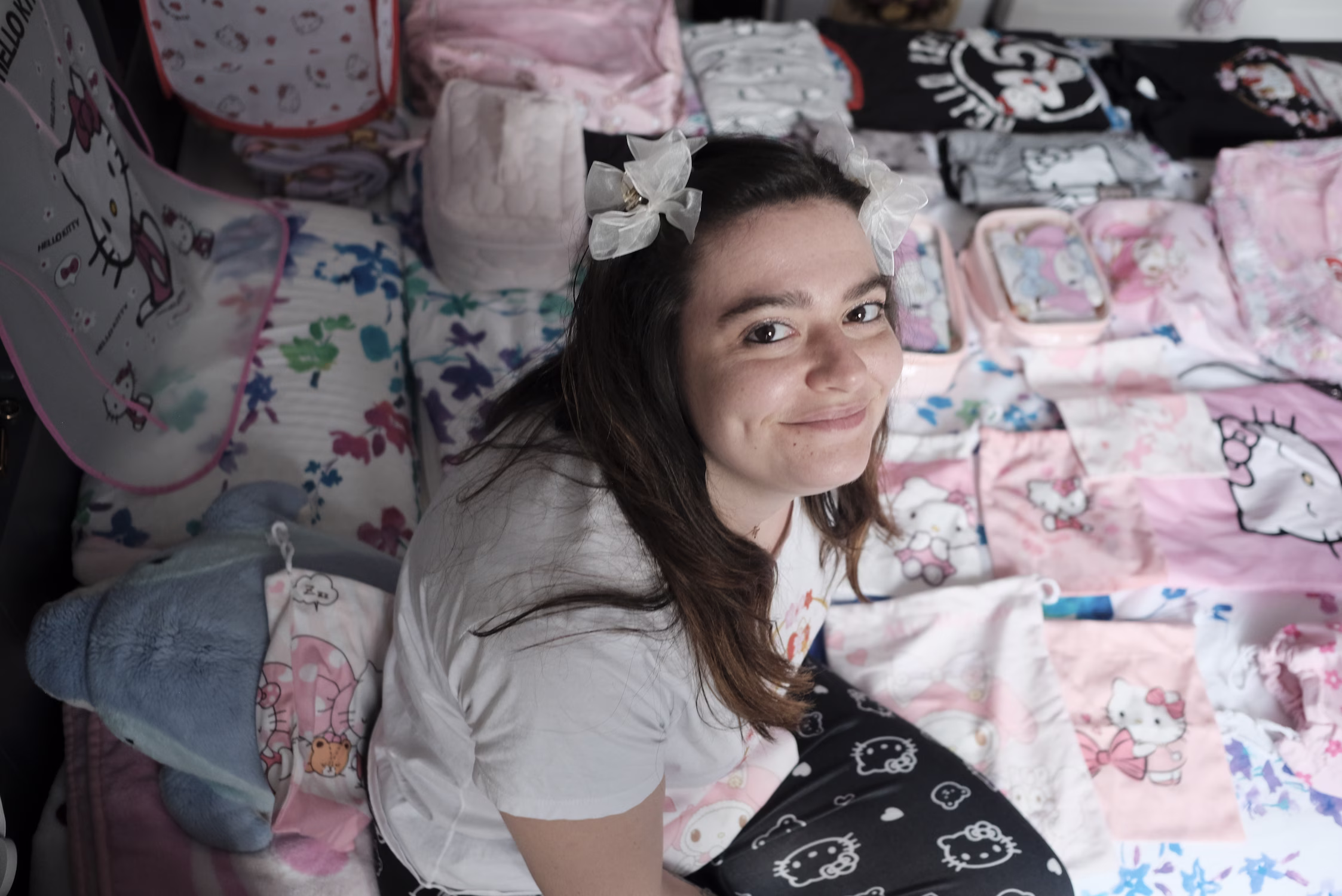 Jeune femme souriante assise parmi des objets et tissus Hello Kitty aux couleurs pastel.