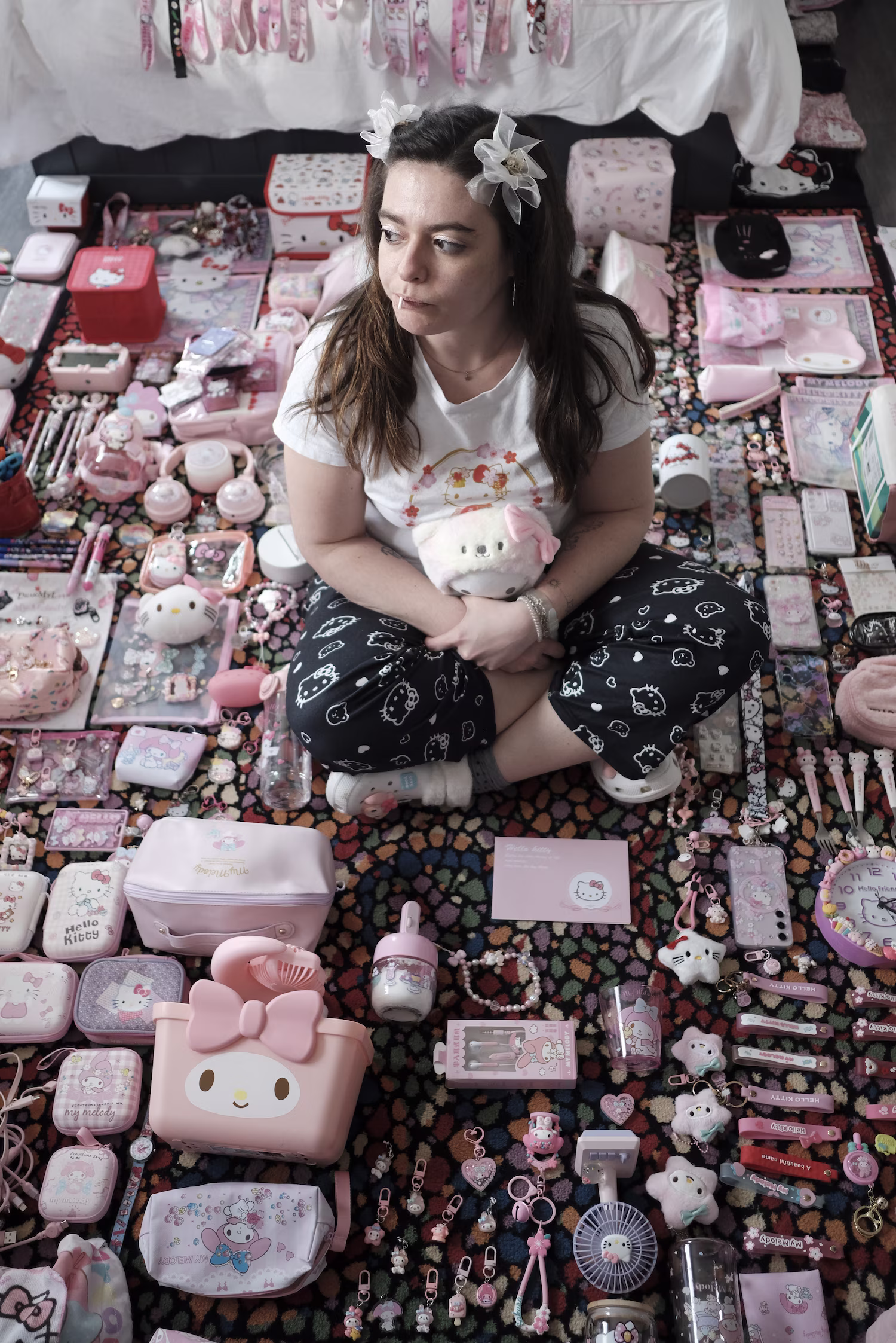 Femme assise entourée de nombreux objets Hello Kitty et Sanrio sur un tapis coloré.