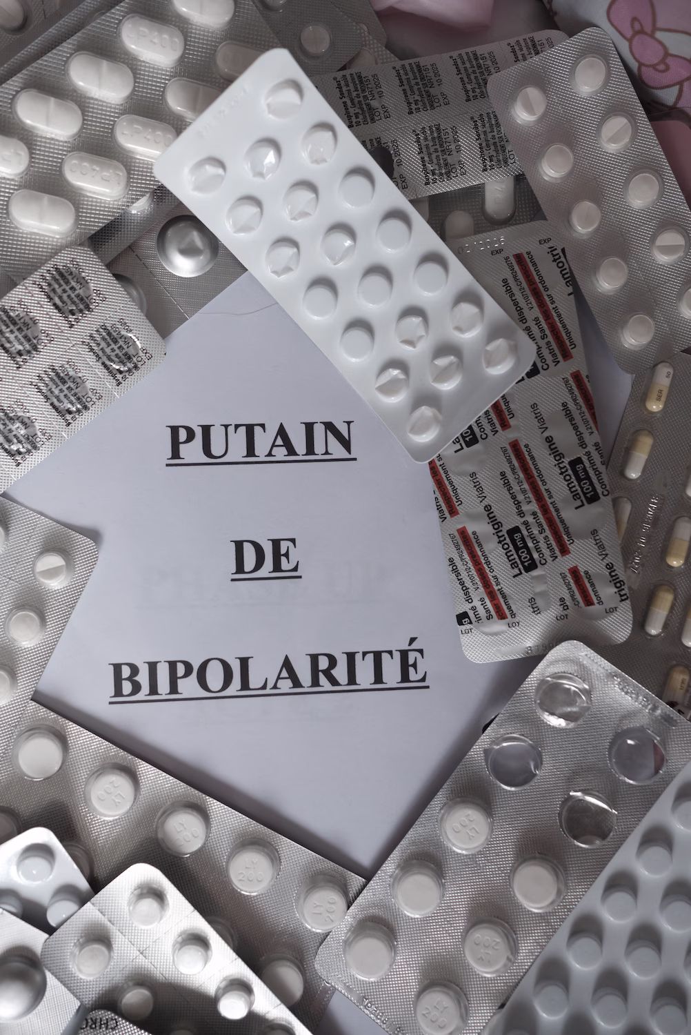 Plaquettes de médicaments blanches entourant un papier marqué « PUTAIN DE BIPOLARITÉ ».