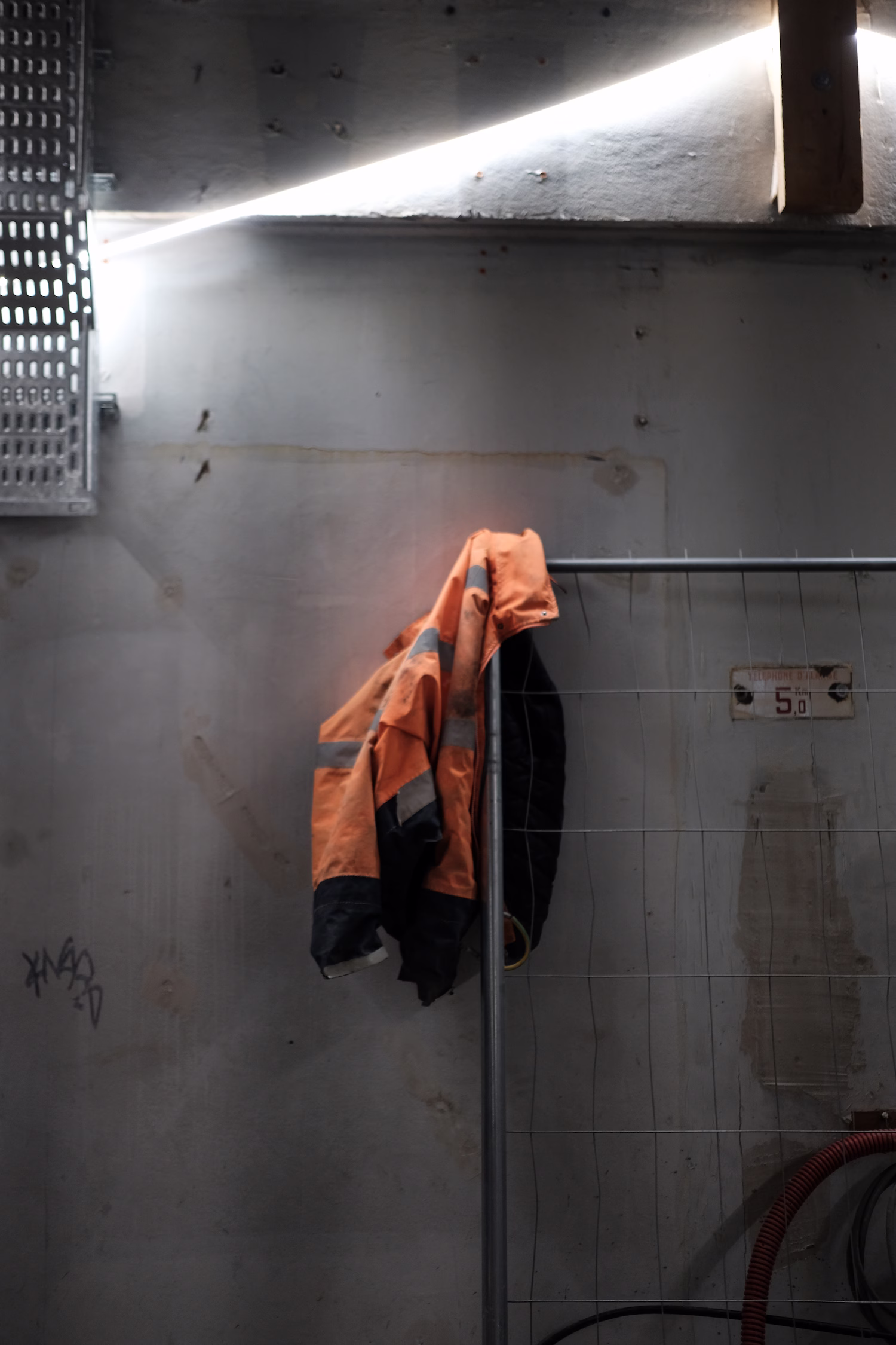 Veste orange de travail suspendue sur une grille métallique dans un espace industriel sombre.