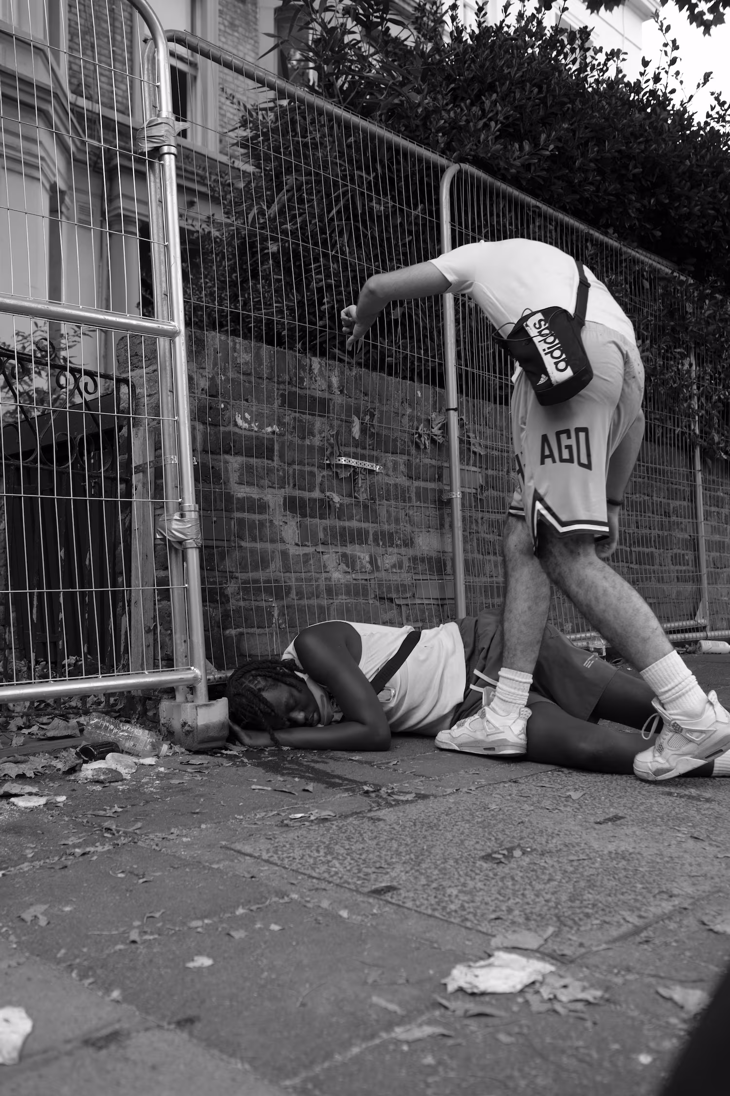 Une personne allongée sur le trottoir près d'une barrière métallique, une autre penchée vers elle.
