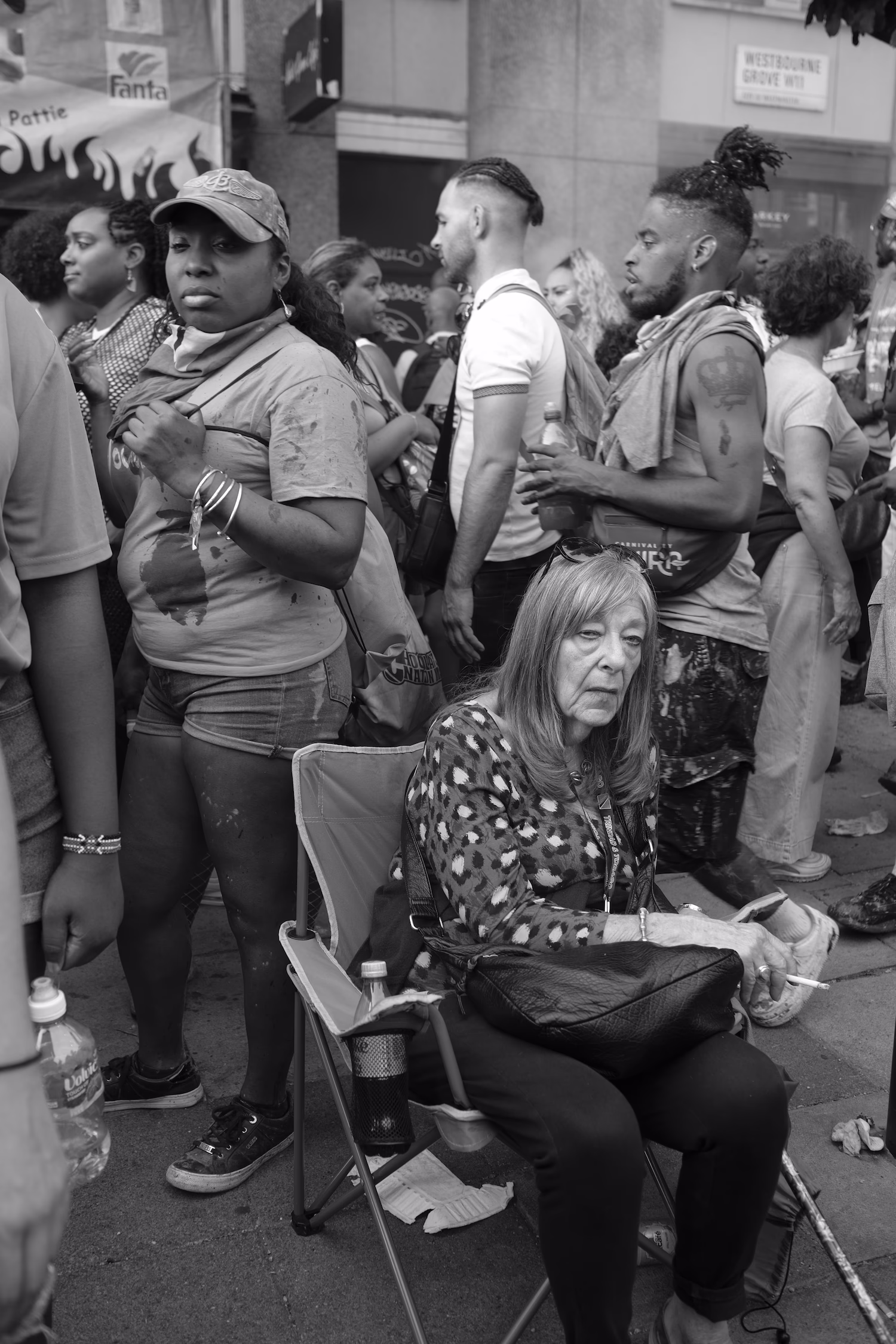 Femme assise sur une chaise pliante entourée de personnes debout dans une foule urbaine.