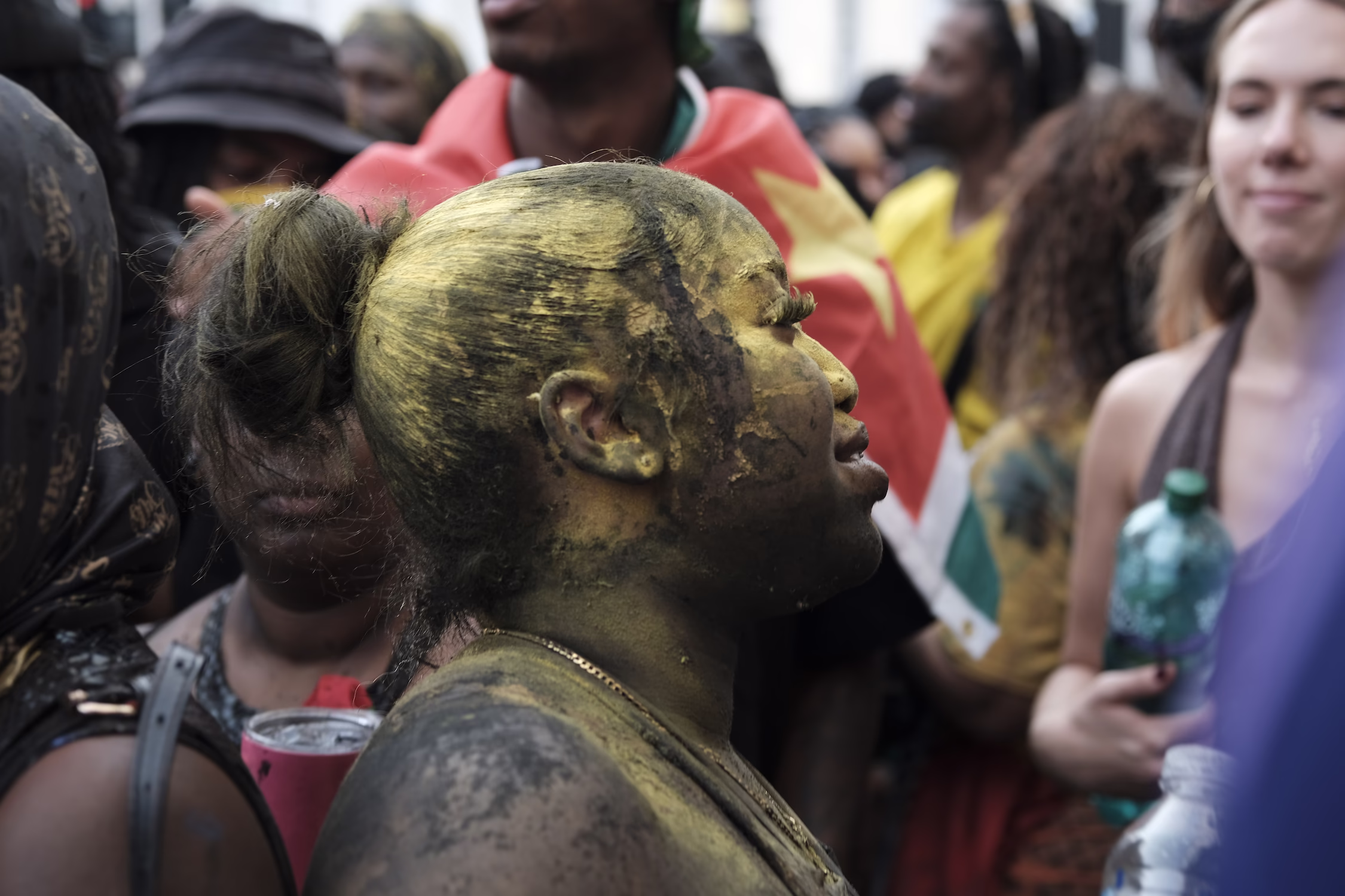 Femme avec visage et corps peints en jaune au milieu d'une foule lors d'une célébration extérieure.