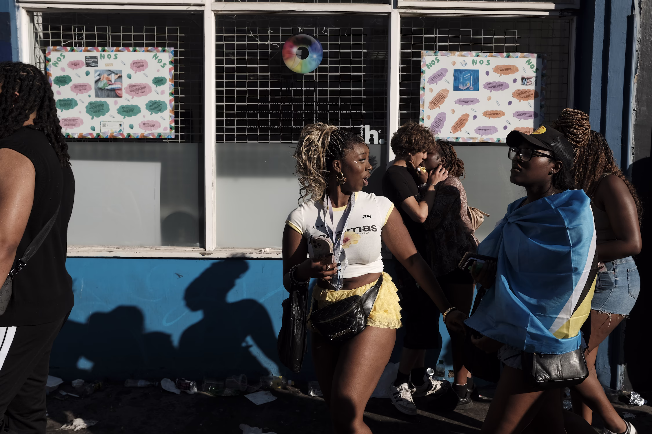 Groupe de jeunes femmes discutant devant une vitrine avec affiches colorées, certaines portant un drapeau.