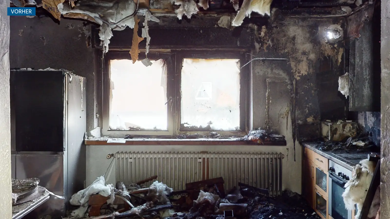 Eine stark verbrannte Küche mit verkohlten Wänden, geschmolzener Isolierung, die von der Decke hängt, zerbrochenen Fenstern und Trümmern auf dem Boden und den Geräten.