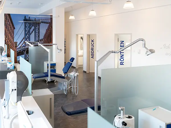 Fertig sanierte Praxisräume mit mehreren Behandlungssektionen, die durch undurchsichtige Glaswände getrennt sind. Der Raum ist hell erleuchtet, im Hintergrund sind Glastüren mit Beschriftungen zu sehen, die in anliegende Behandlungszimmer führen.