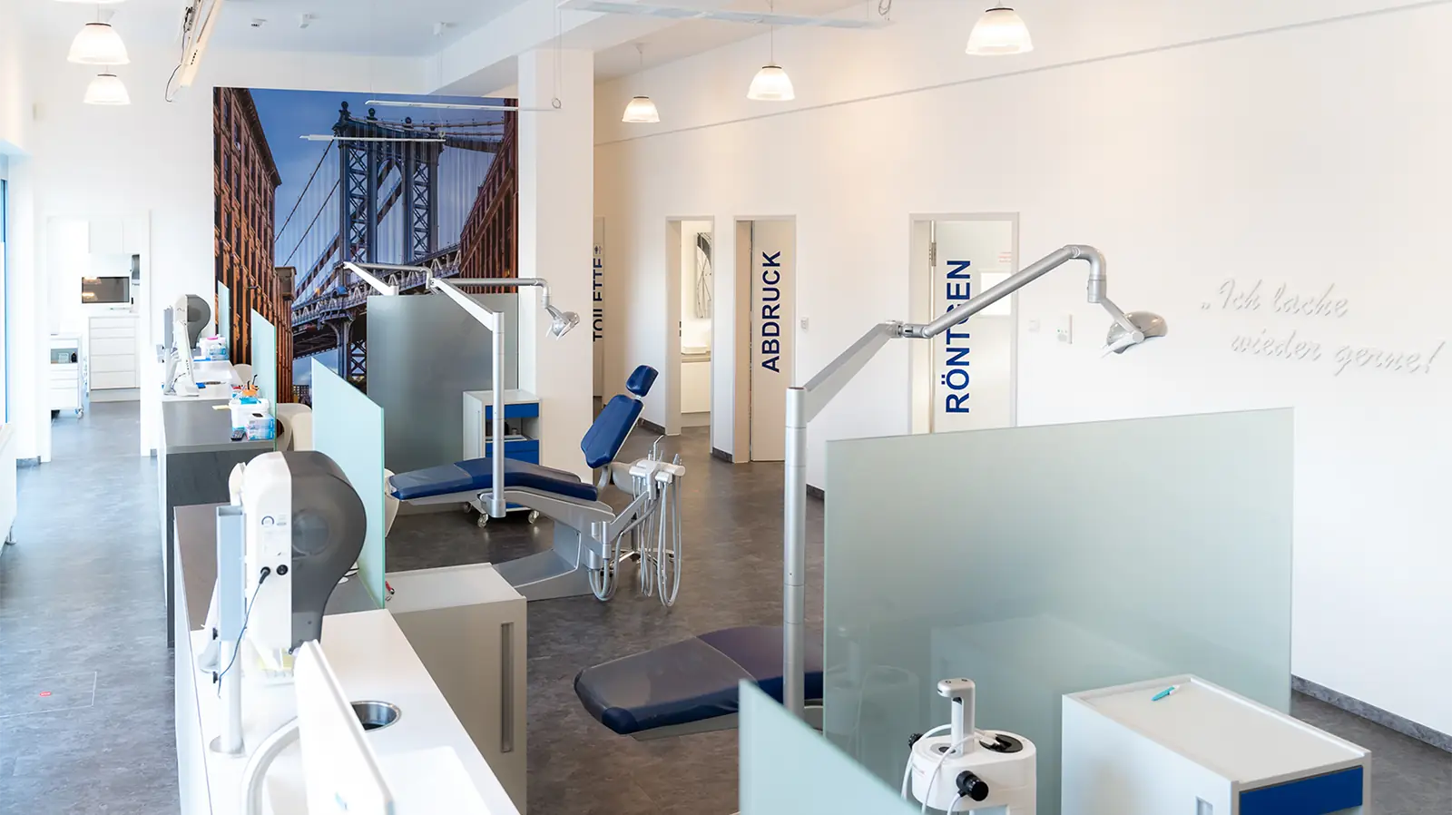 Fertig sanierte Praxisräume mit mehreren Behandlungssektionen, die durch undurchsichtige Glaswände getrennt sind. Der Raum ist hell erleuchtet, im Hintergrund sind Glastüren mit Beschriftungen zu sehen, die in anliegende Behandlungszimmer führen.
