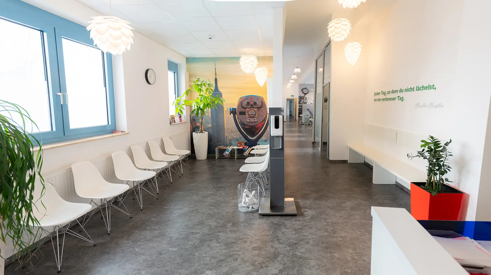 Fertiger Eingangsbereich einer Zahnarztpraxis nach Sanierungsarbeiten. Auf der linken Seite ist der Wartebereich mit zehn weißen Stühlen und einer grünen Pflanze zu sehen, auf der rechten Seite ist ein Flur mit einer weißen Bank an der Wand.