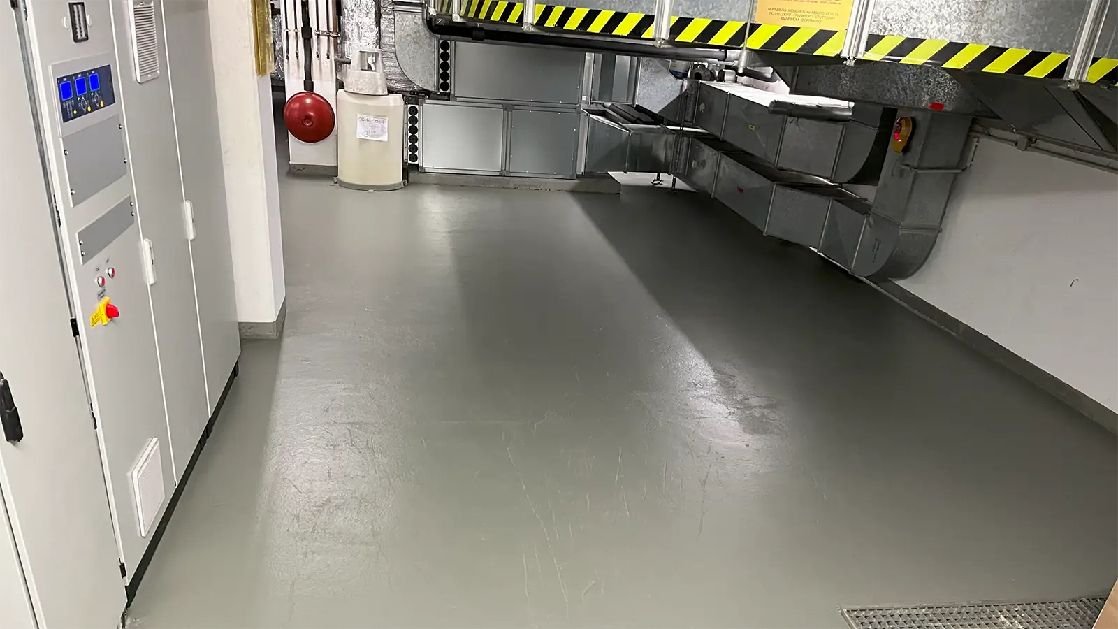 Einer der Technikräume nach der Sanierung. Der Boden wurde neu gemacht, es sind teilweise neue technische Geräte und Gebäudetechnik zu sehen. Im Vordergrund liegen noch Gitterabdeckungen für Bodenvertiefungen.