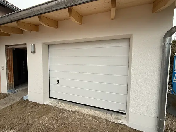 Das Bild zeigt die fertig sanierte Fassade und Garage. Die Tür neben der Garage wurde noch nicht fertiggestellt und das Mauerwerk ist durch den Türrahmen zu sehen.