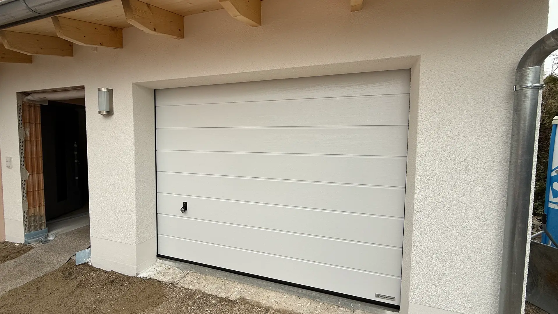 Das Bild zeigt die fertig sanierte Fassade und Garage. Die Tür neben der Garage wurde noch nicht fertiggestellt und das Mauerwerk ist durch den Türrahmen zu sehen.