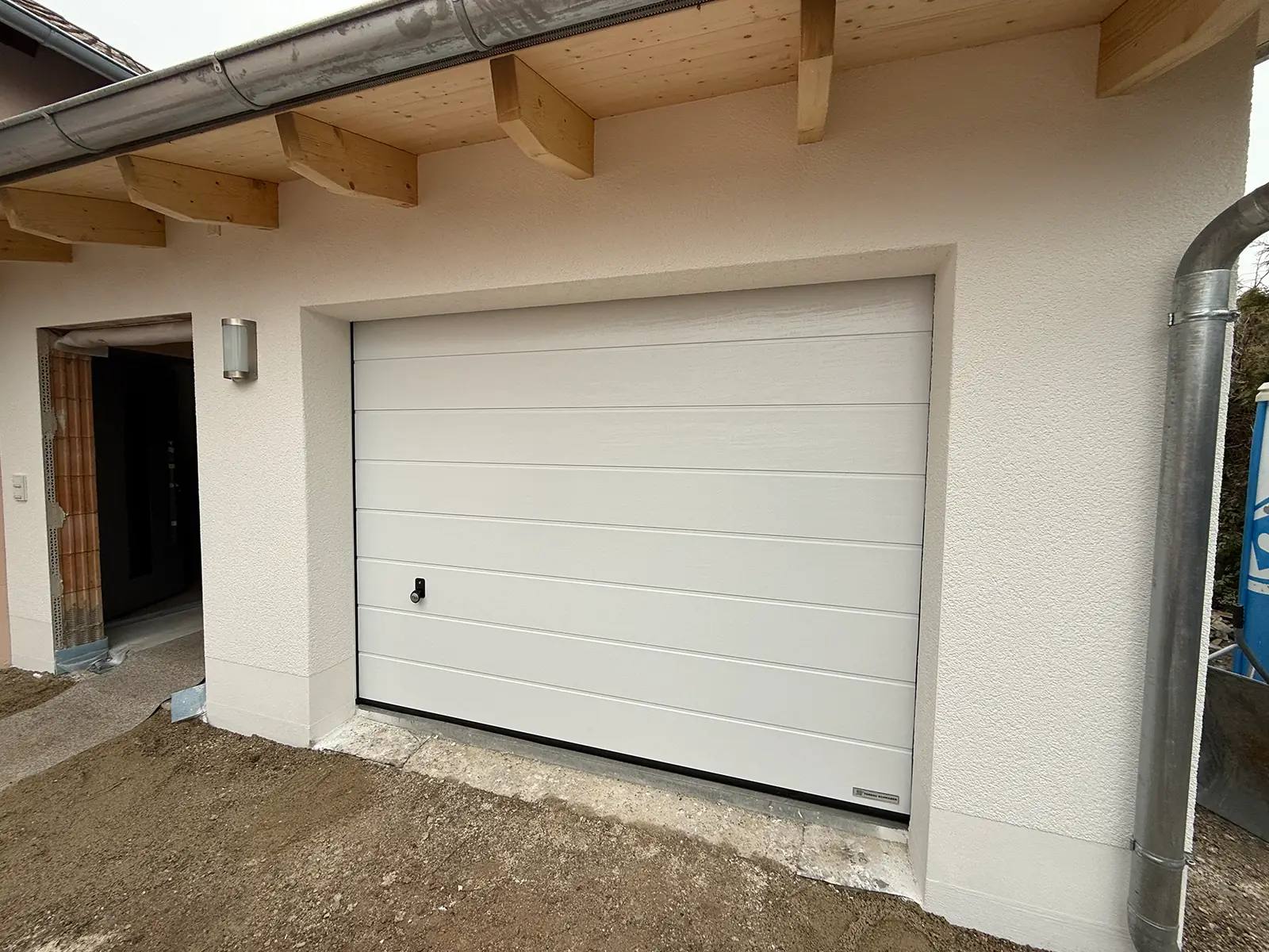 Das Bild zeigt die fertig sanierte Fassade und Garage. Die Tür neben der Garage wurde noch nicht fertiggestellt und das Mauerwerk ist durch den Türrahmen zu sehen.