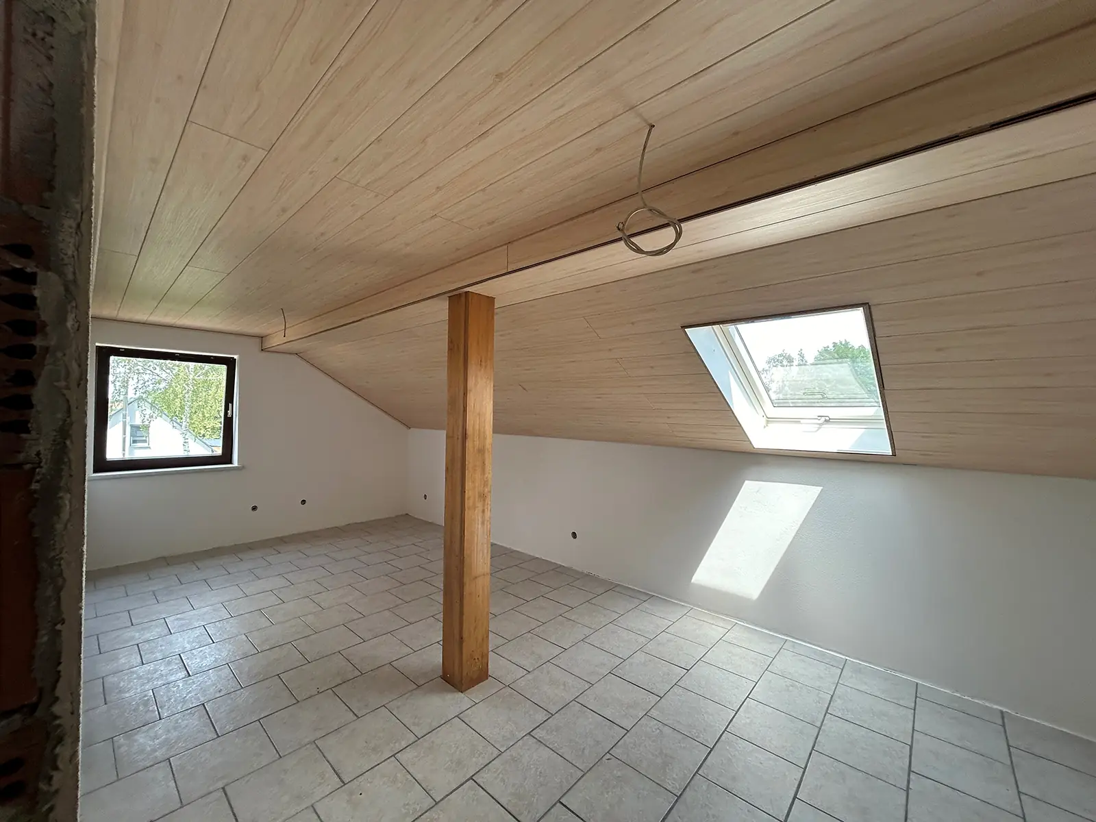 Innenansicht eines der sanierten Räume. Die Decke ist mit hellem Holz verkleidet, die Wand weiß gestrichen und der Boden weiß gefliest. Durch die Fenster scheint Licht und erhellt den Raum.