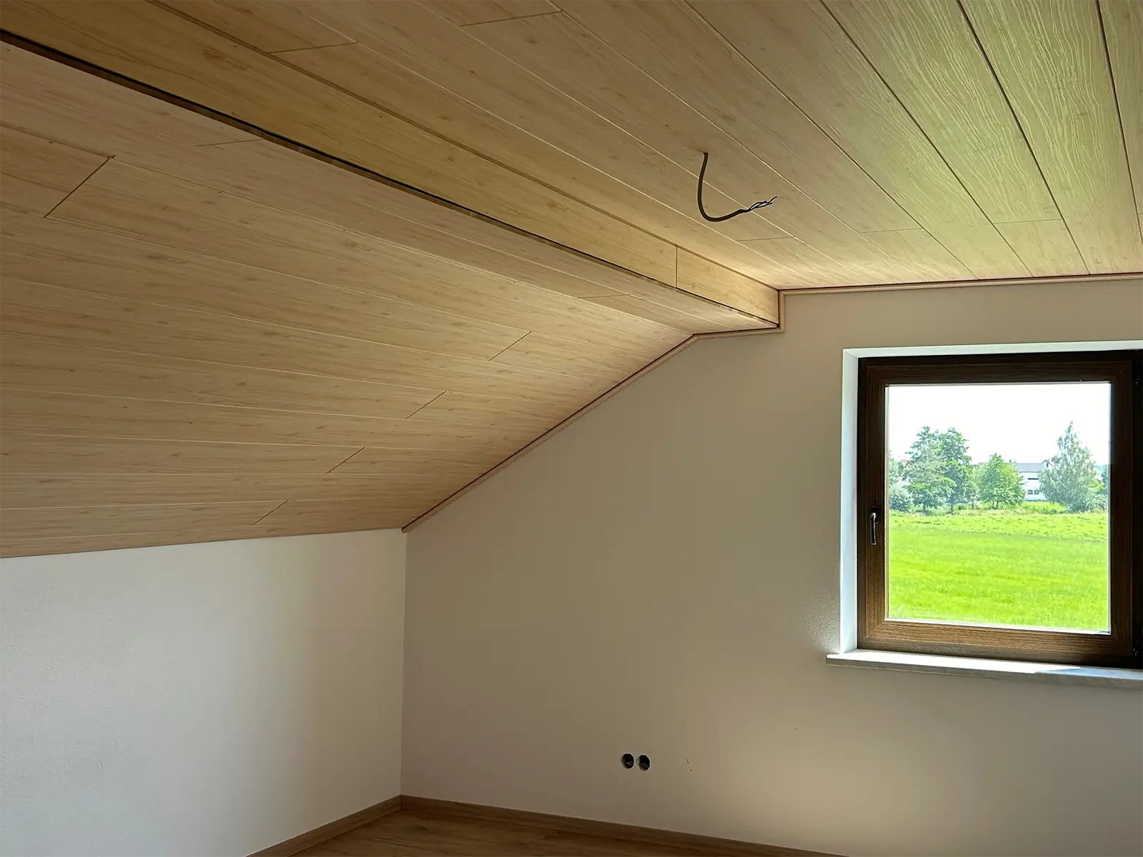Innenansicht eines sanierten Raums. Ein Fenster auf der Stirnseite wirft Licht in den Raum. An der Decke ist die neue Holzverkleidung zu erkennen, die Wände sind weiß gestrichen.