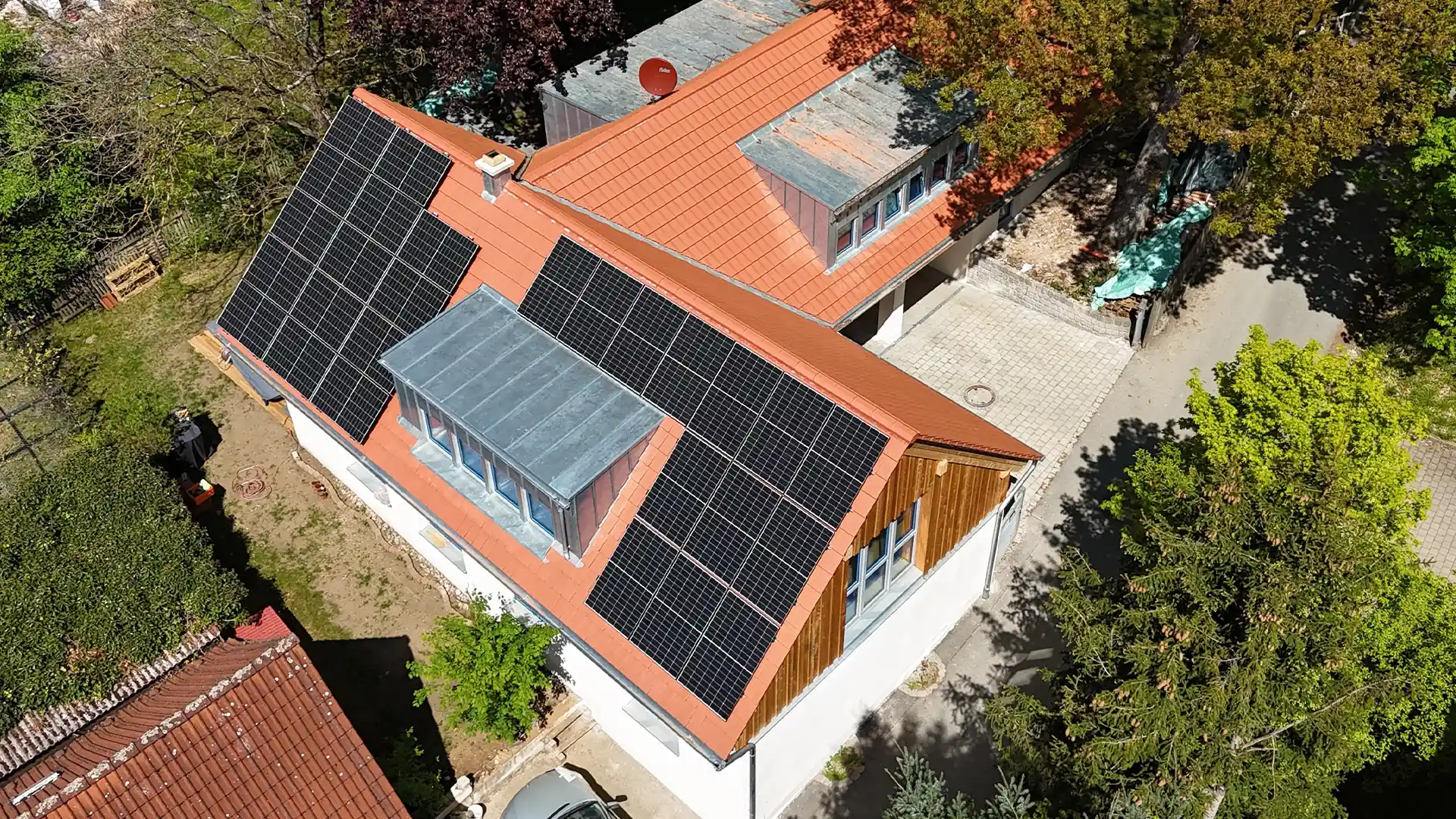 Vogelperspektive des sanierten Hauses. Auf dem Dach mit roten Ziegeln sind flächendeckend Solarzellen angebracht. Um das Gebäude sind die Zufahrt, Gärten und viele Bäume zu erkennen.
