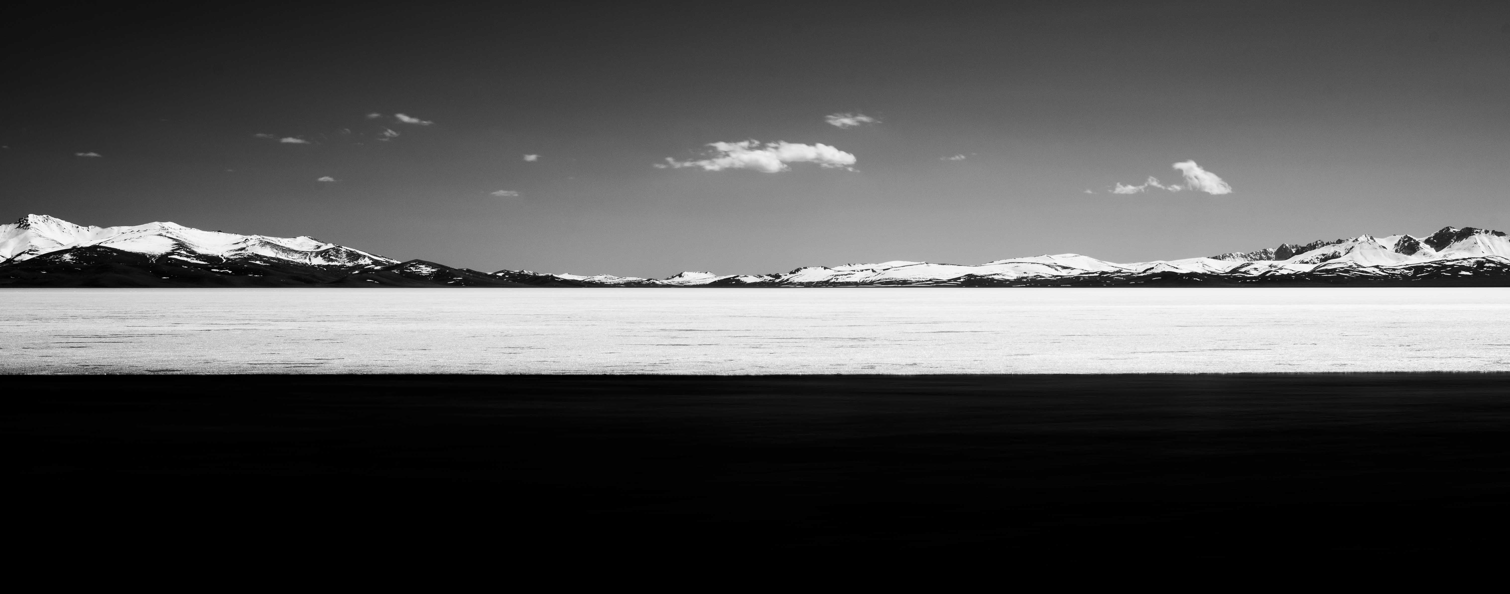 Black and white panoramic view of snow-covered mountains under a clear sky with a few clouds.