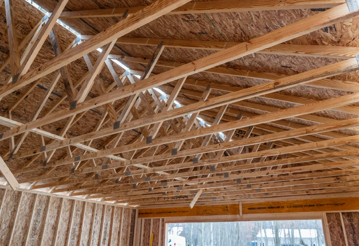 Interior view of a building under construction showing wooden roof trusses and partially framed walls.
