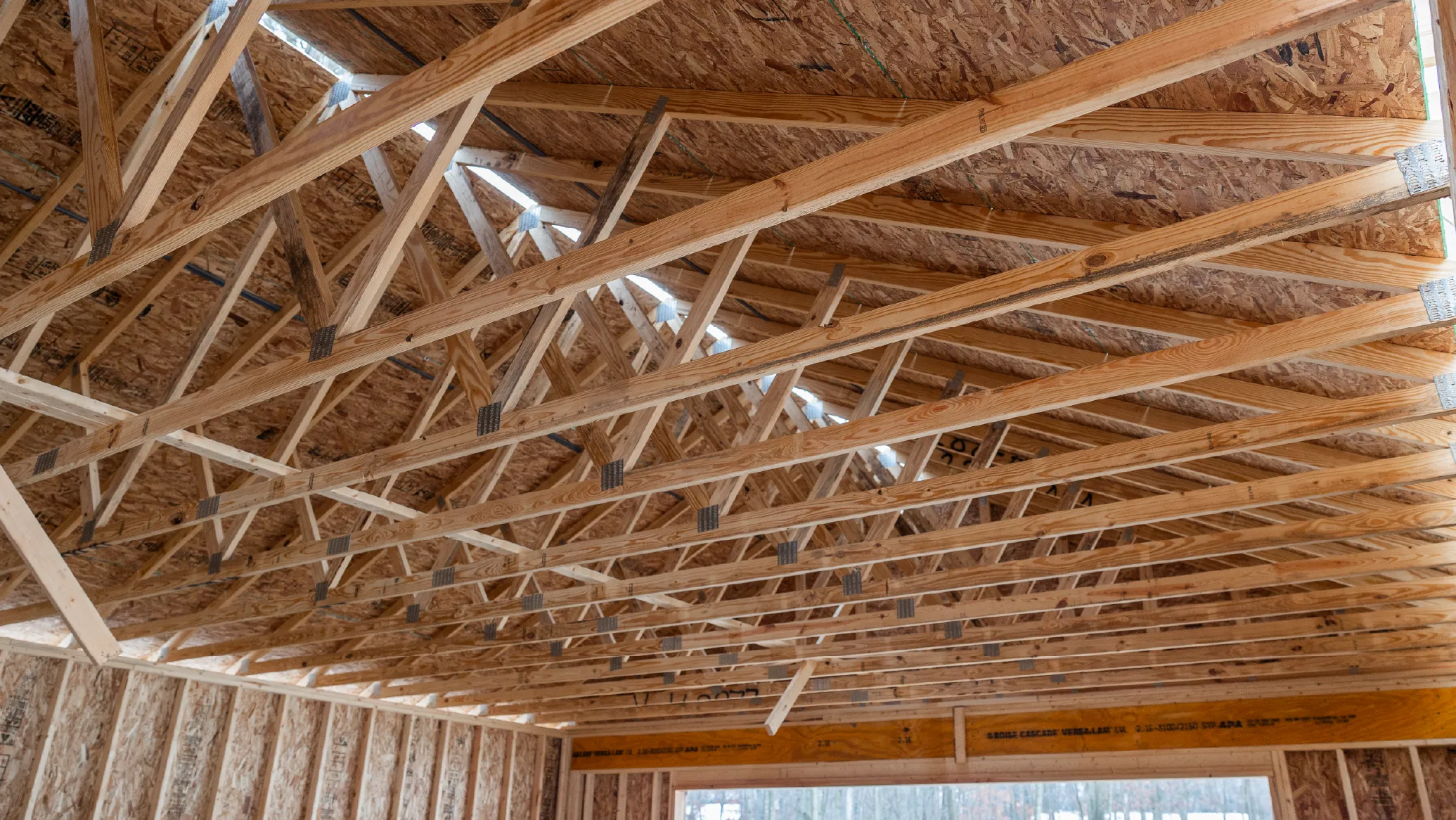 Interior view of a wooden roof structure with exposed trusses and beams in a building under construction.