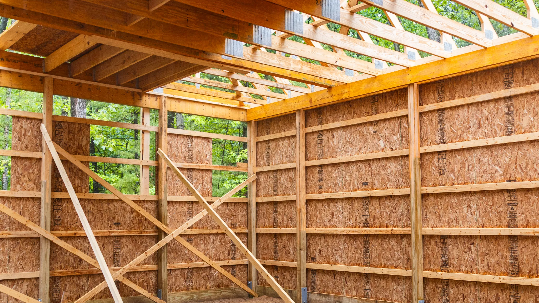 Interior framework of a wooden barn under construction with exposed beams and plywood walls.