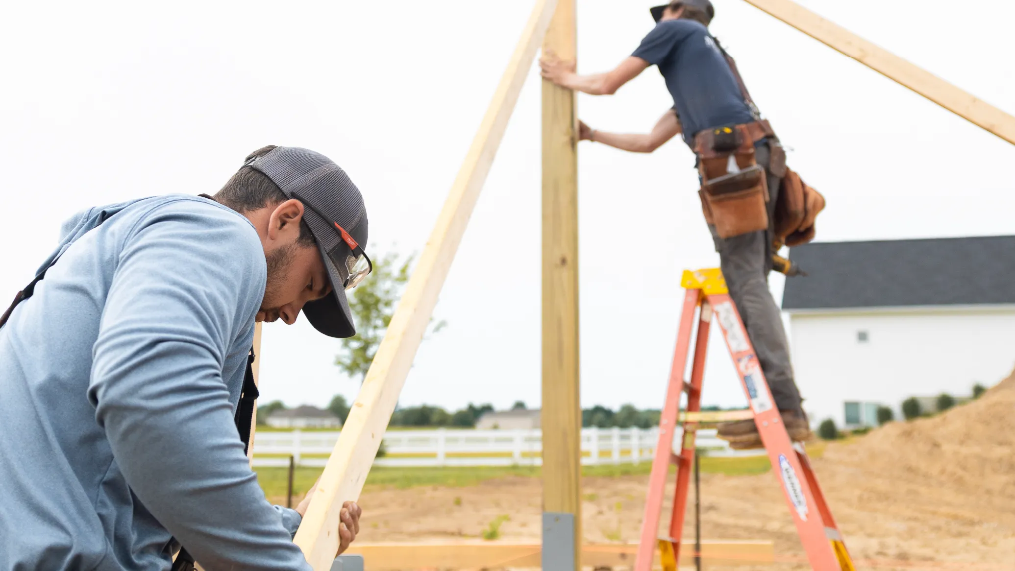 Two construction workers assembling wooden beams for an outdoor structure on a building site.