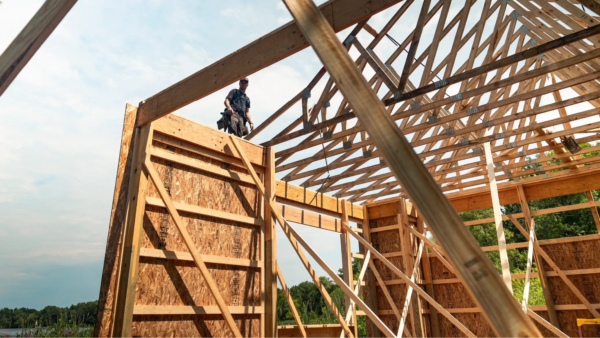Construction worker standing on the wooden frame of a barn under a partly cloudy sky.