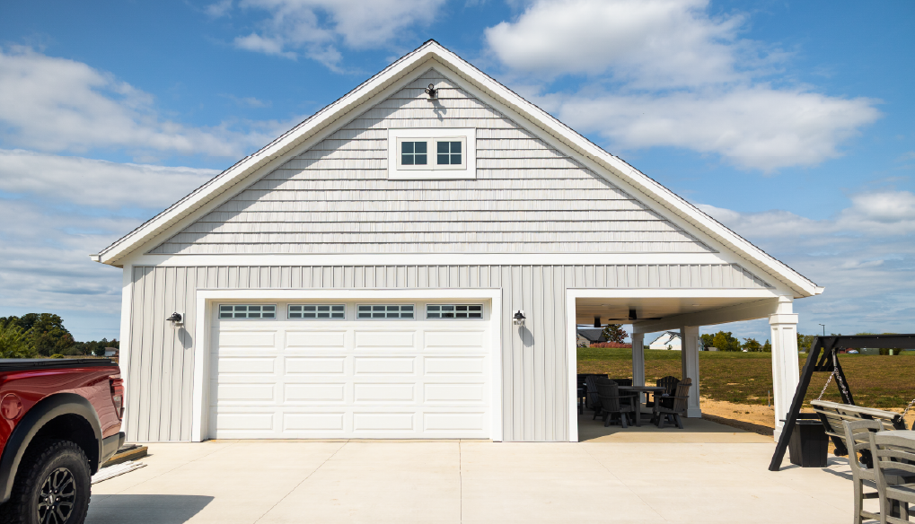 White detached garage with a closed double garage door and an open covered patio area with chairs and a table under a blue sky.