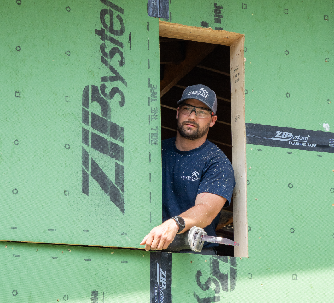 Construction worker wearing safety glasses and a McKellar shirt installing a window frame on a building with ZIP System green sheathing.