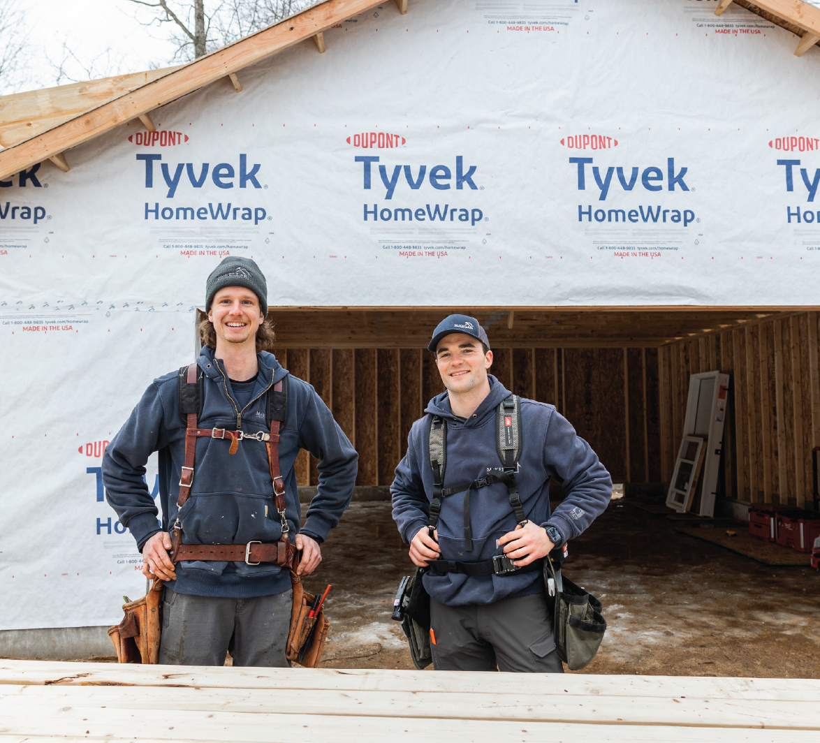 Two construction workers in tool belts standing in front of an unfinished building wrapped with Tyvek HomeWrap.
