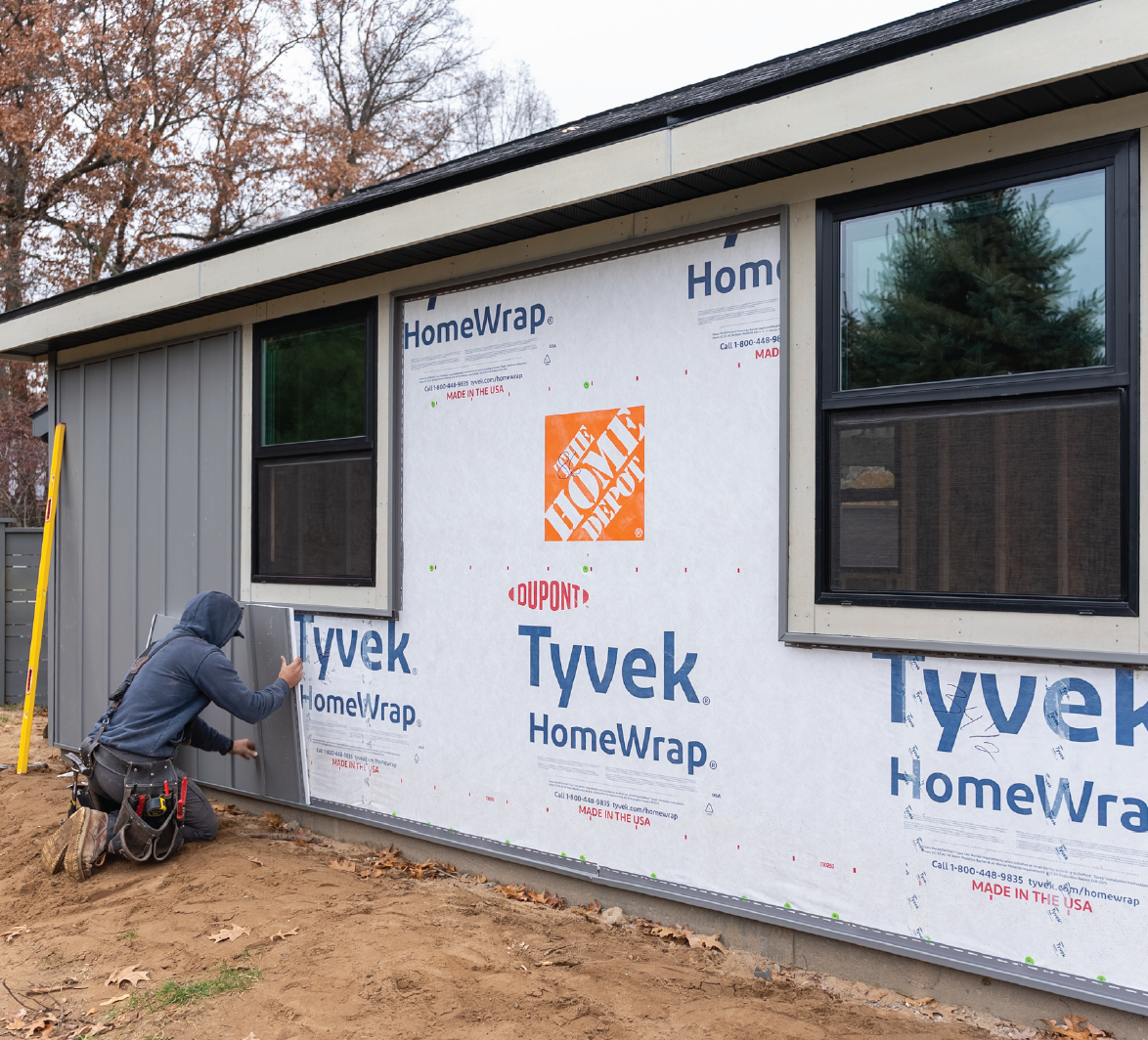 Construction worker installing grey siding on a house exterior over Tyvek HomeWrap weather barrier.