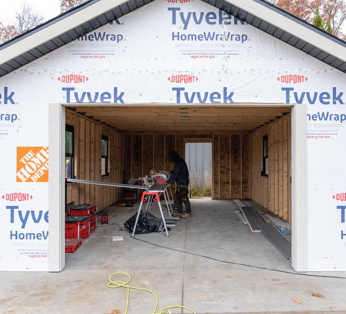 Person cutting metal strips inside an unfinished garage with Tyvek HomeWrap on exterior walls.