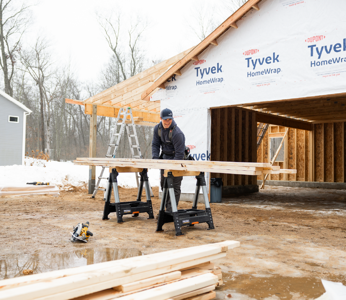 Construction worker measuring wooden planks outside a partially built house wrapped with Tyvek HomeWrap.