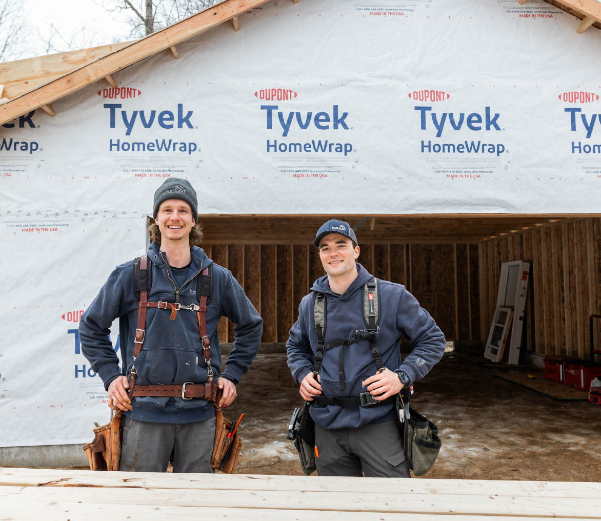 Two male construction workers wearing tool belts and work clothes standing in front of a building under construction wrapped with Tyvek HomeWrap.
