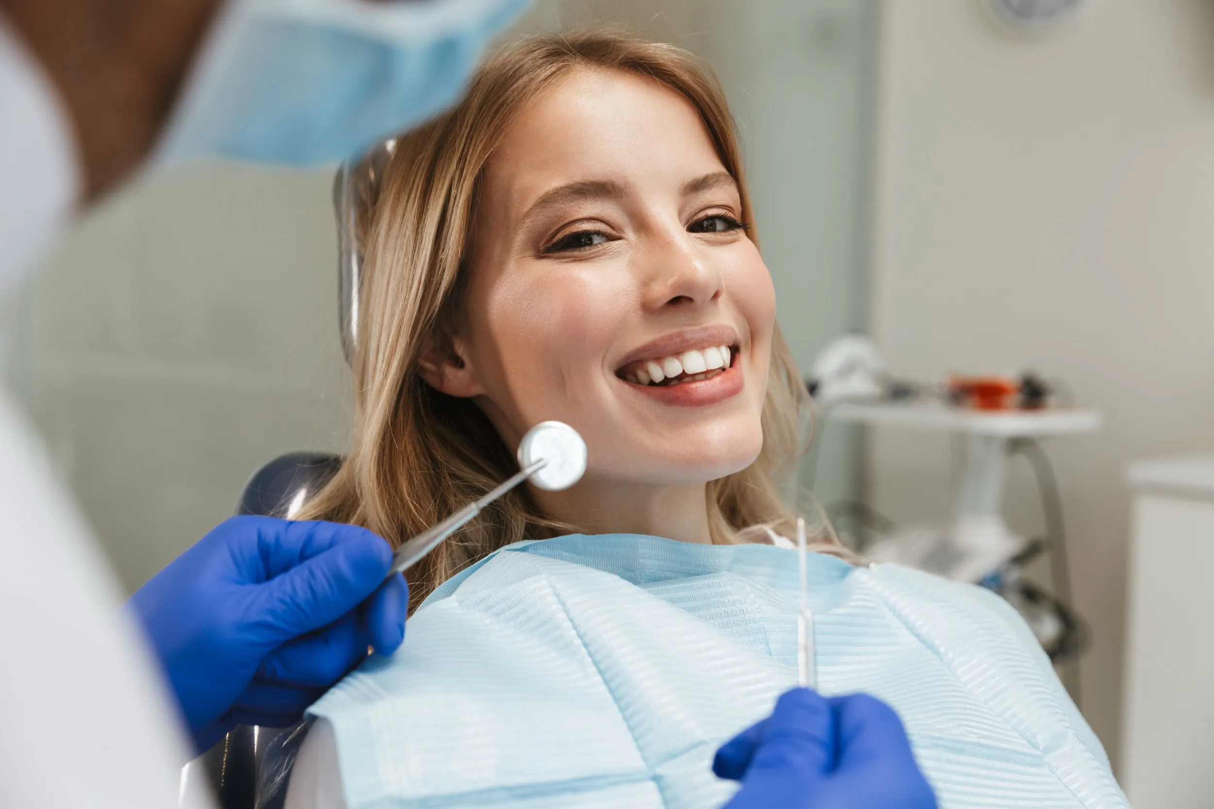Smiling patient during dental checkup with dentist's blue gloved hands