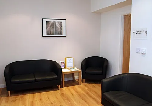 Minimalist waiting room with black chairs, wooden floor, and framed artwork