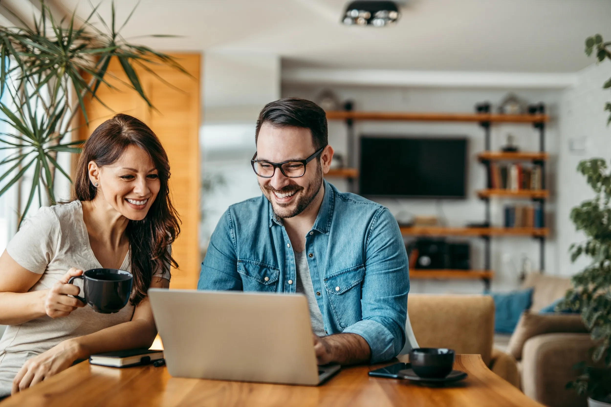 Two people smiling and working together on a laptop at home