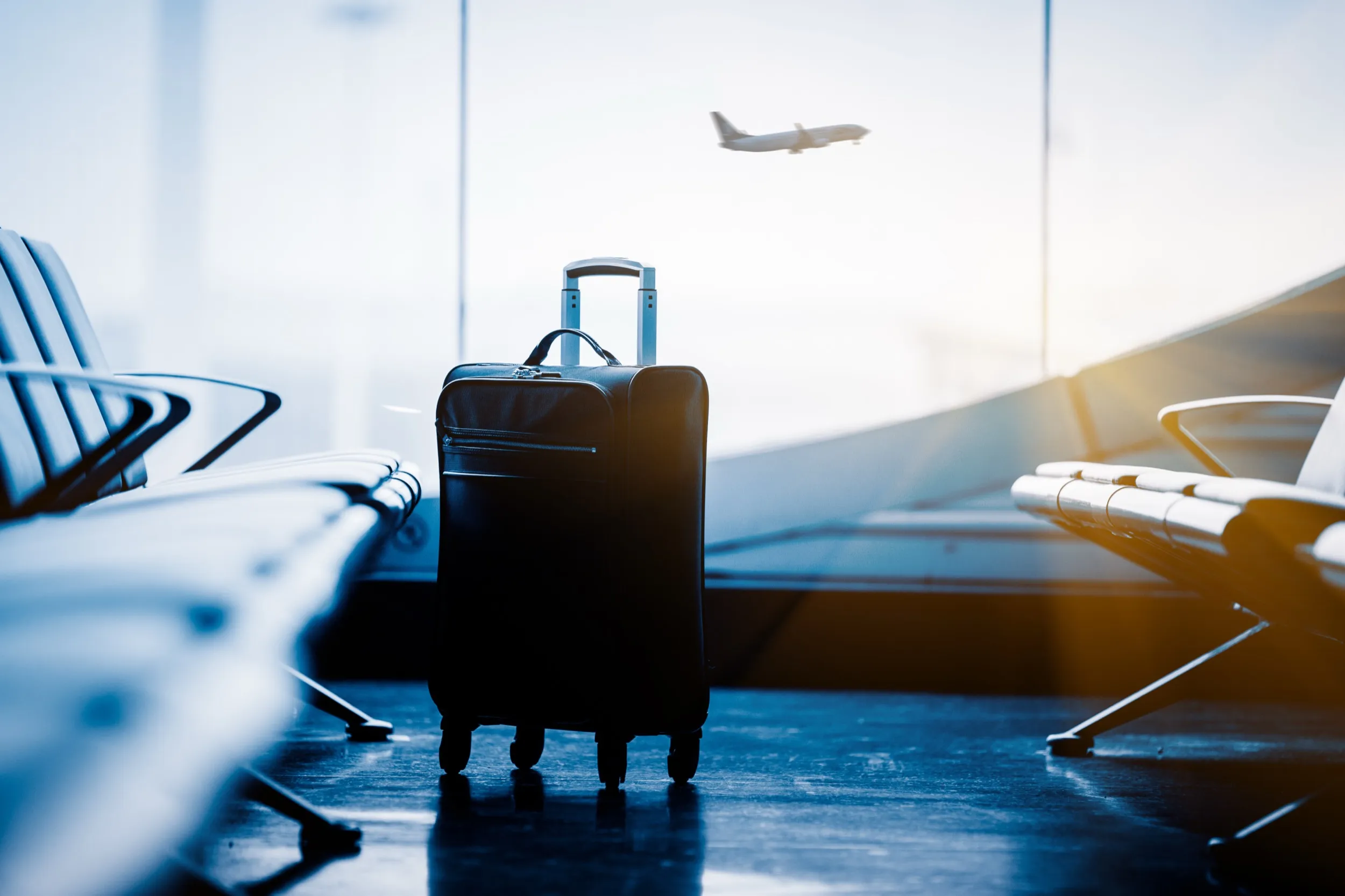 Suitcase in airport terminal with airplane taking off in background