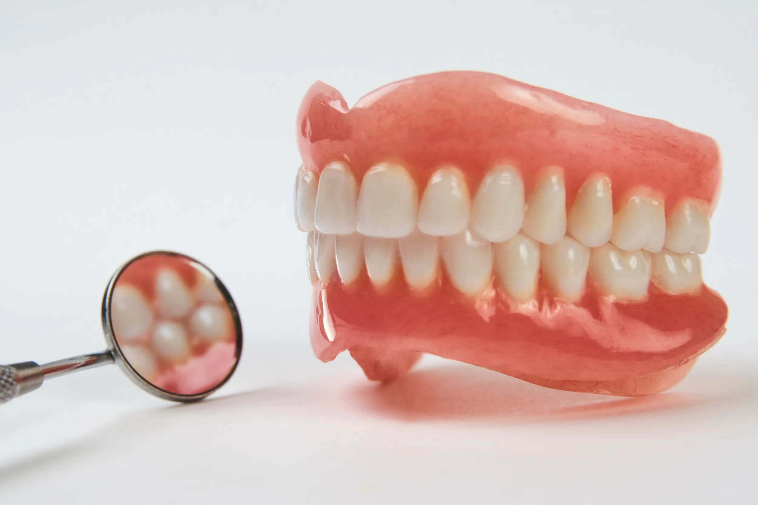 Full set of dentures with dental mirror on white background