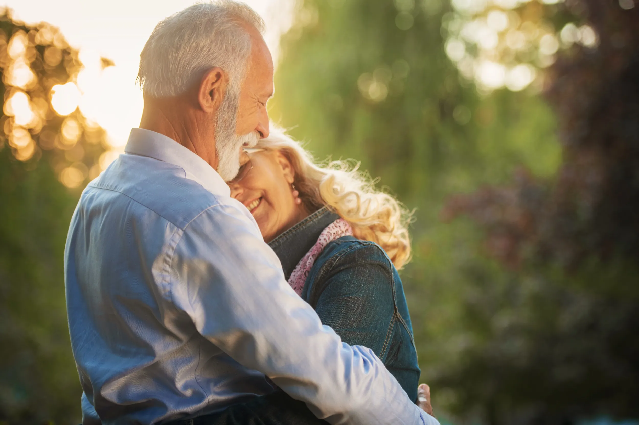 Older couple hugging tenderly in warm, soft sunlight outdoors