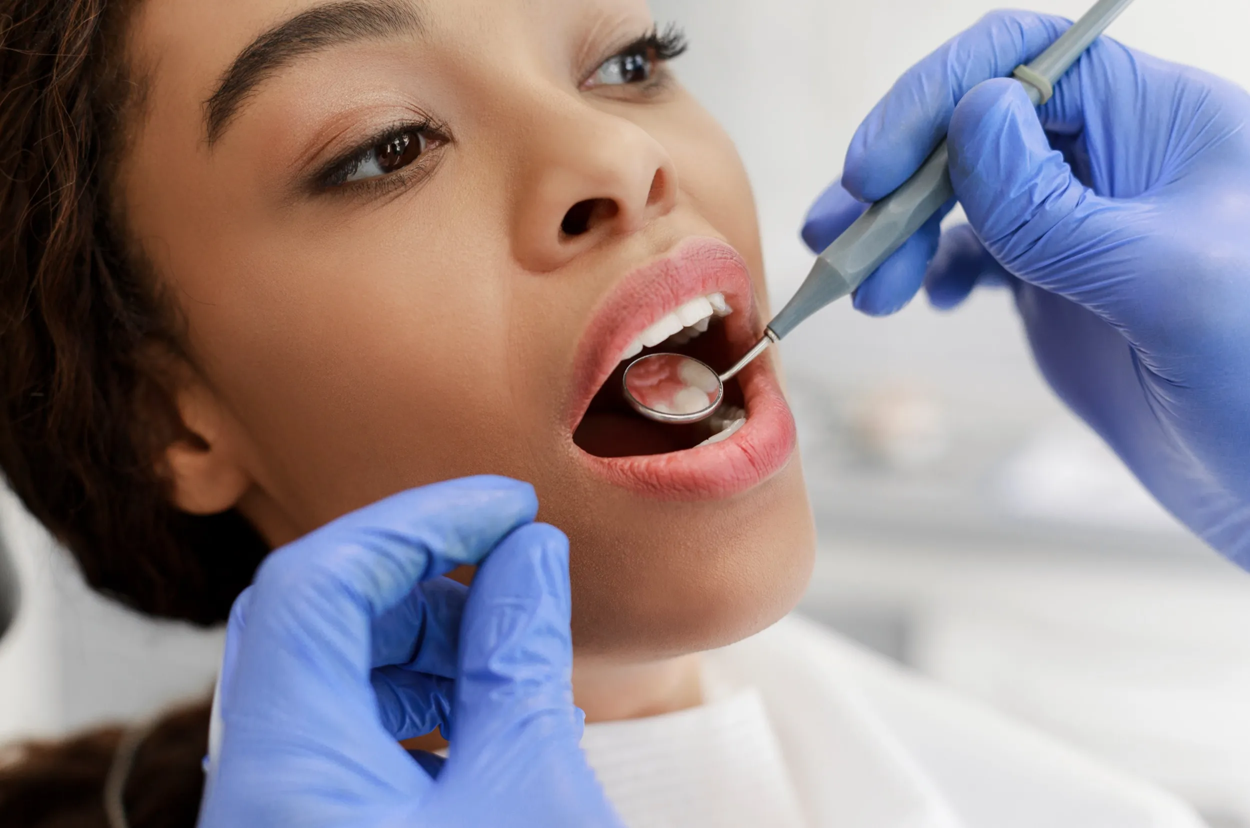 Dentist examining patient's teeth with dental mirror and gloved hands