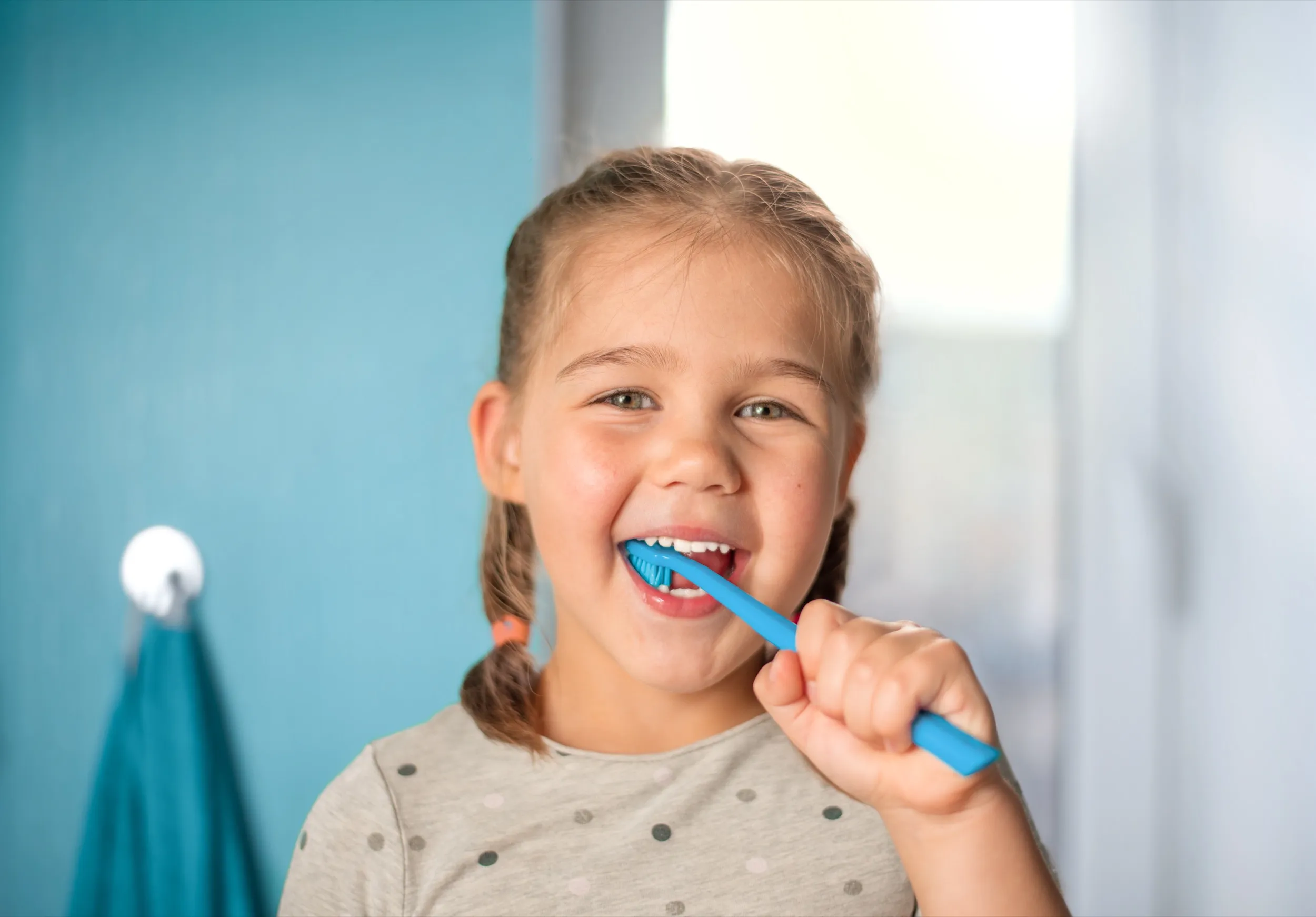 Smiling child brushing teeth with blue toothbrush in bathroom