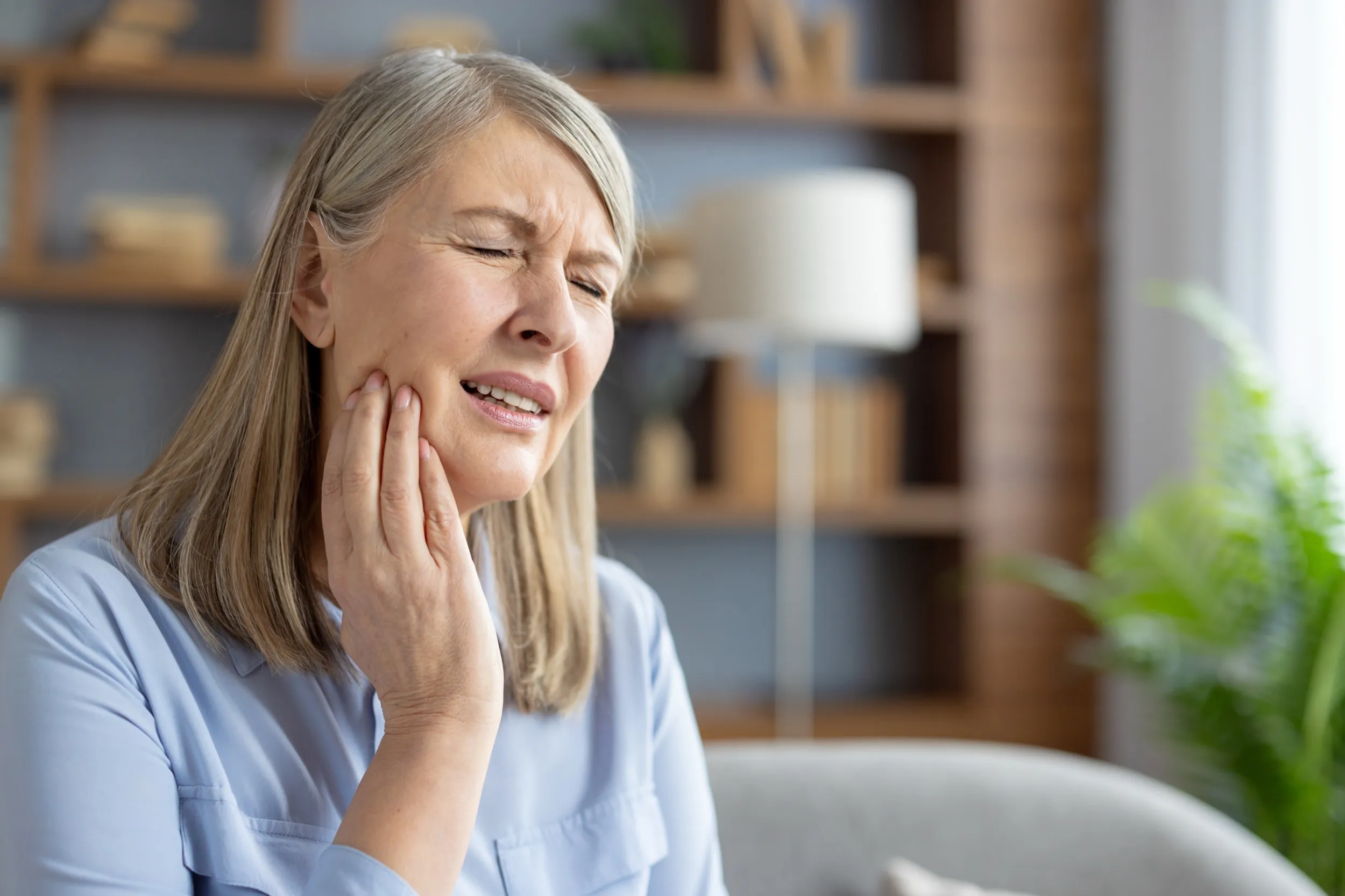 Woman experiencing tooth pain, holding cheek with eyes closed