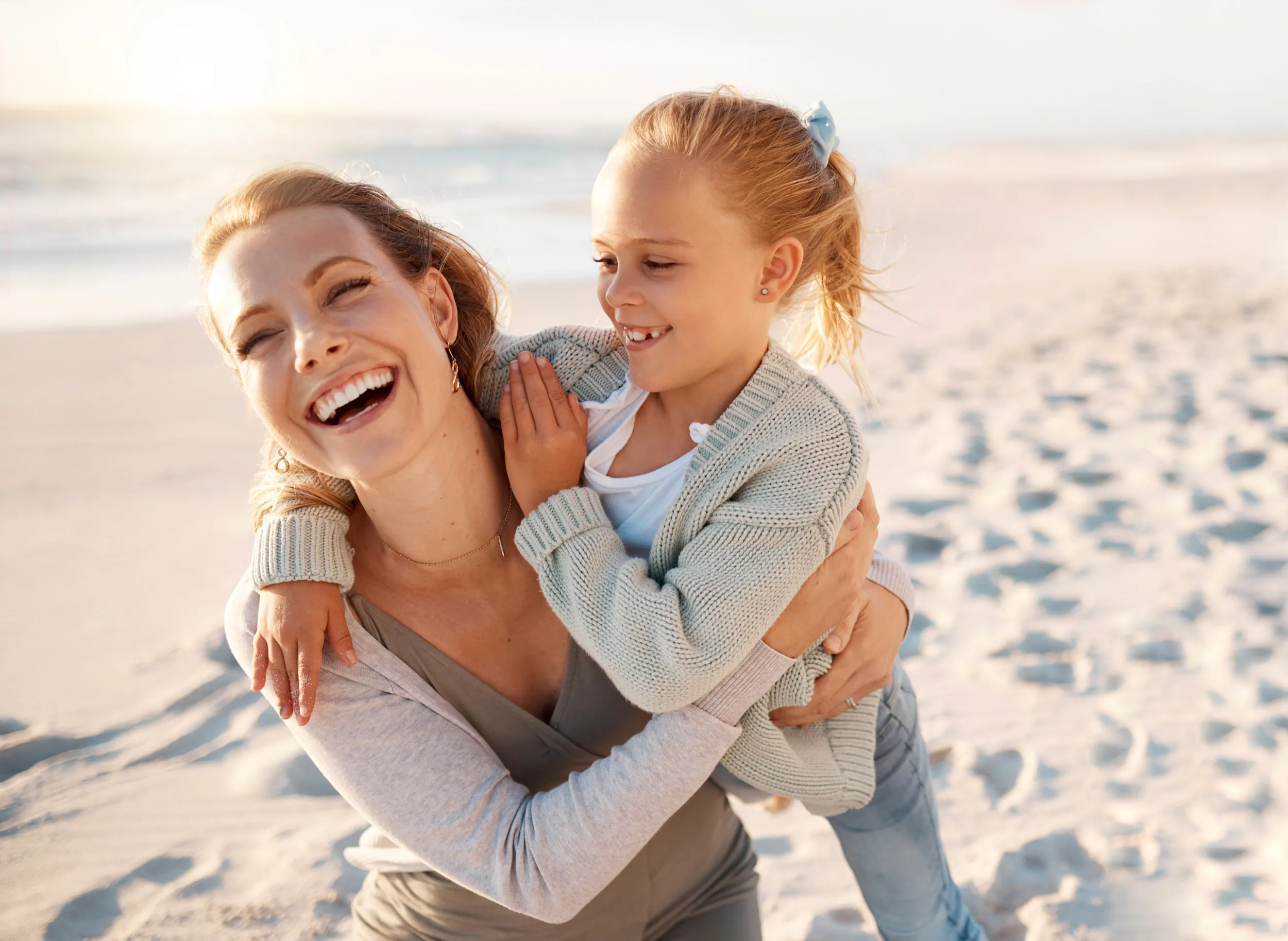 Mother and daughter laughing together on sandy beach in matching sweaters
