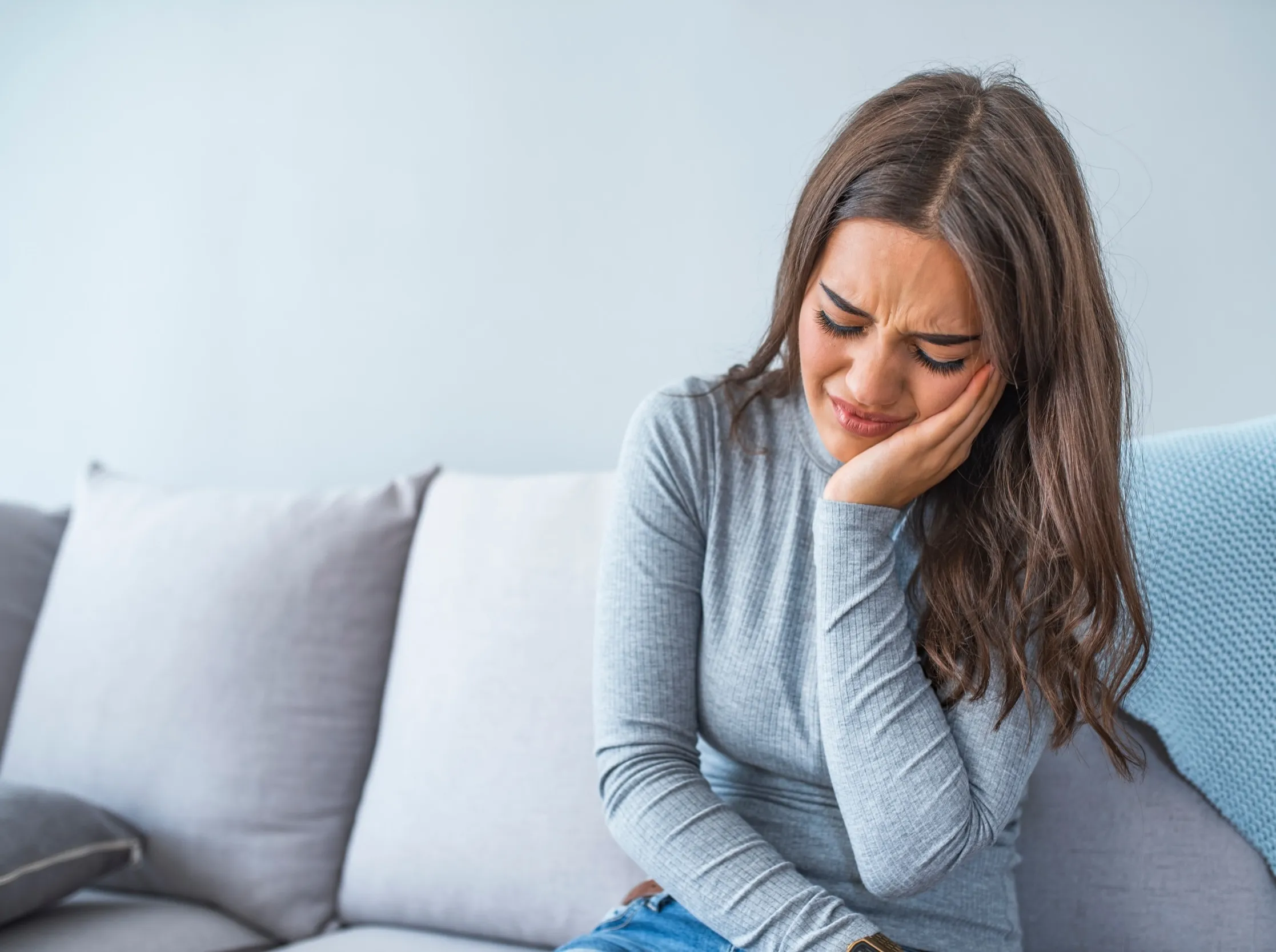 Woman with pained expression resting head on hand on couch